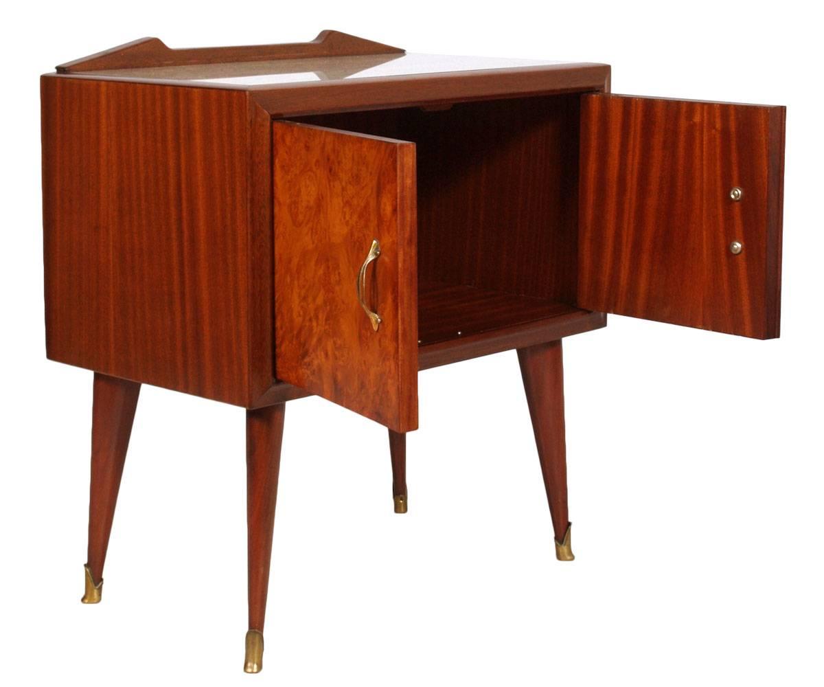 Mid-Century Modern pair of bedside table or nightstands in solid mahogany, mahogany and elm burl veneered. Glass top with a musical score decorative paper. Backsplash top shaped. Handles and feet in golden brass. In excellent conditions. Wax