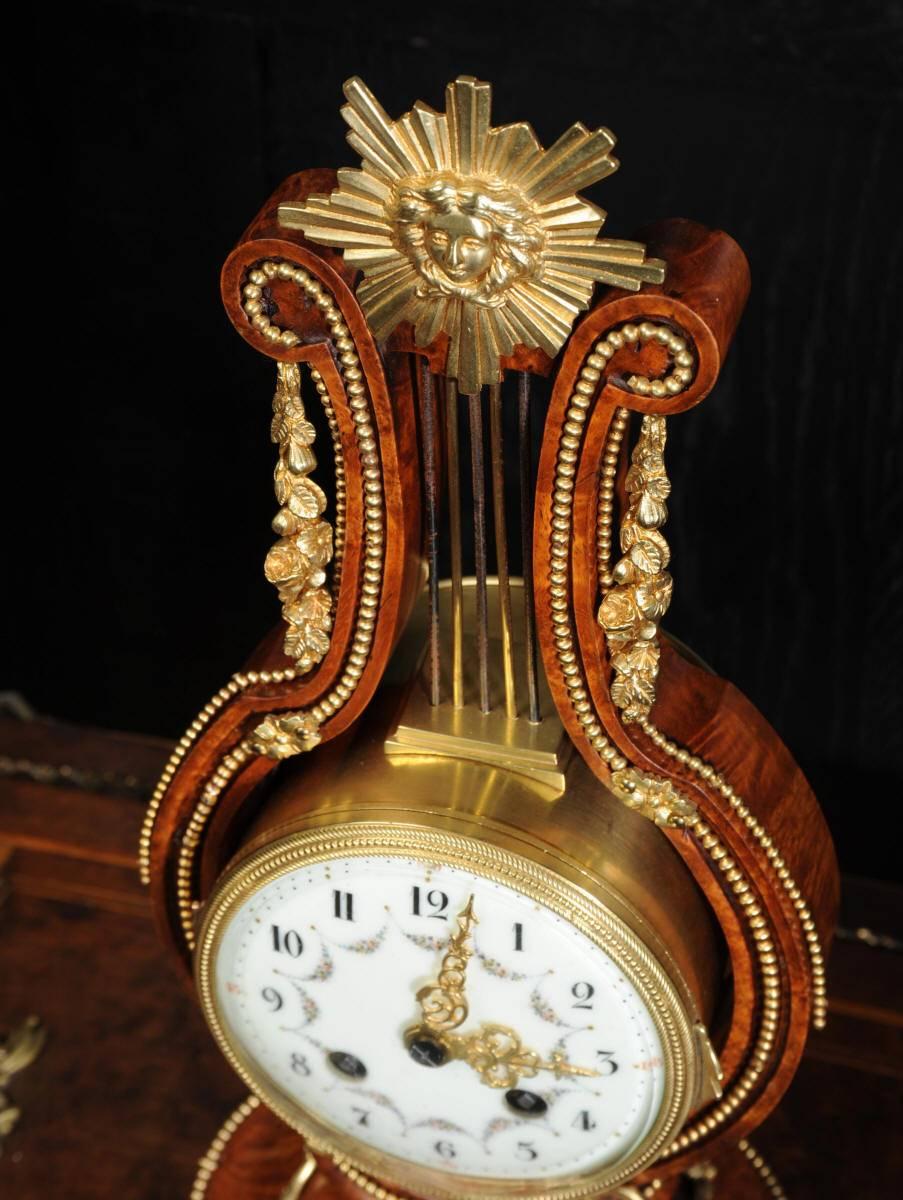 An exquisite small sized boudoir or desk clock, beautifully formed in the sought after Louis XVI lyre shape. It is finely figured walnut mounted with ormolu (Fine gilded bronze). To the top is a sunburst motif with the brass and blued steel