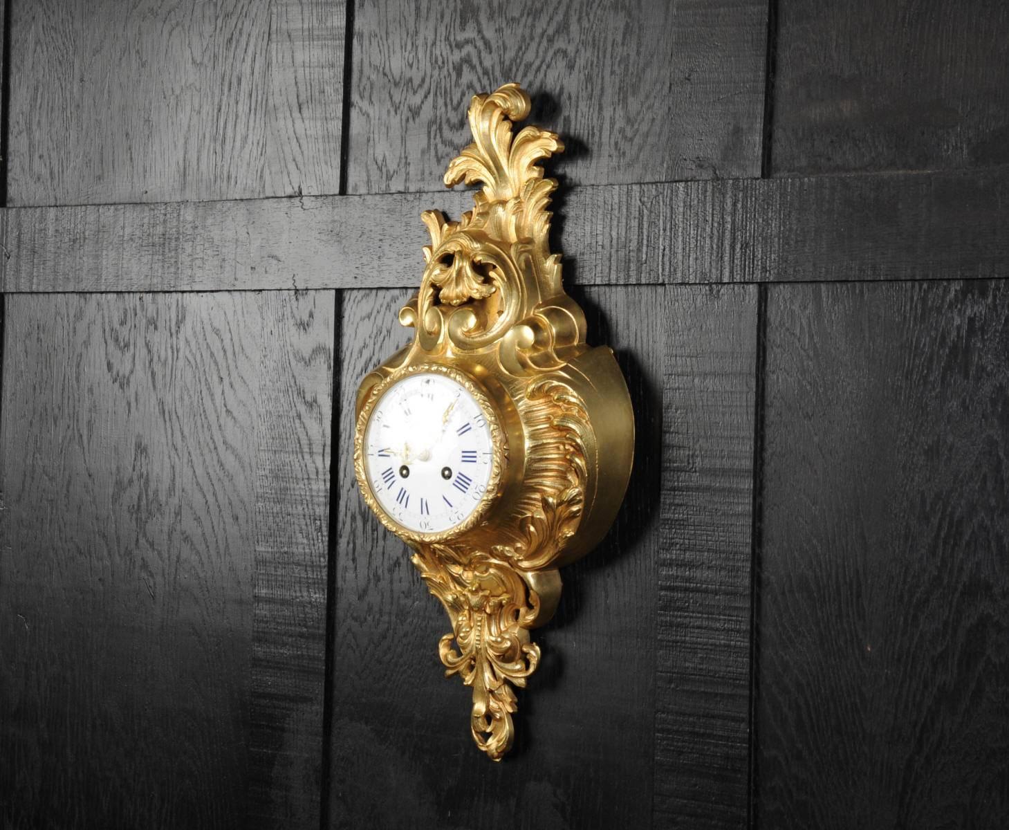 A very decorative antique French gilt bronze Cartel wall clock by Samuel Marti. It is Rococo in style, asymmetric with acanthus shoulders and a large acanthus leaf top. Acanthus flowers hang below the dial. It is in stunning condition, finely