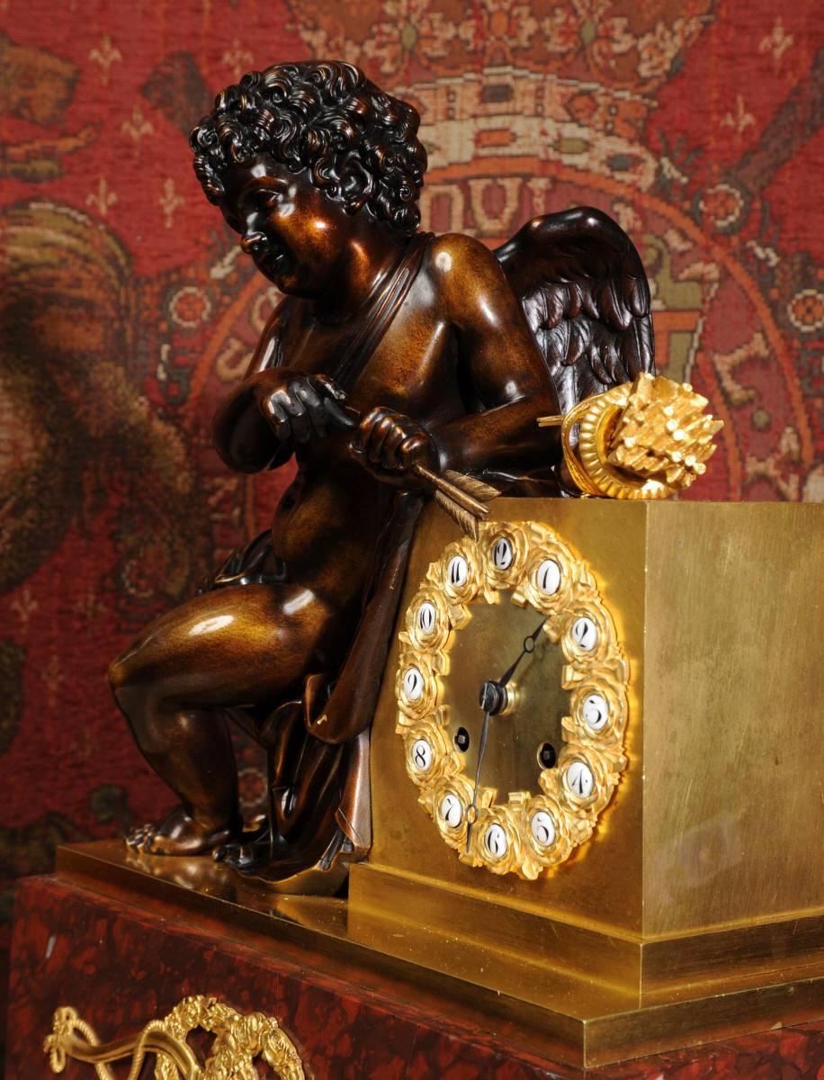 A large, fine and exquisite, early antique French clock depicting cupid holding a sharpened golden arrow. It is of stunning quality and fully serviced and tested by our clockmakers. It is of finest ormolu (finely gilded bronze or bronze doré)