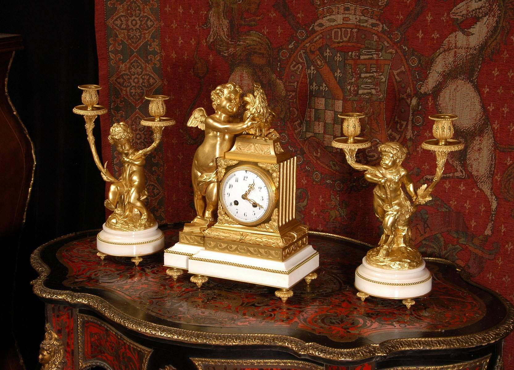 A very fine and stunning ormolu (finely gilded bronze) and white marble clock set in the Louis XVI style. Exquisitely modelled, this is a large, heavy and finely detailed set. It features a putto standing on a pile of books, playfully grabbing a