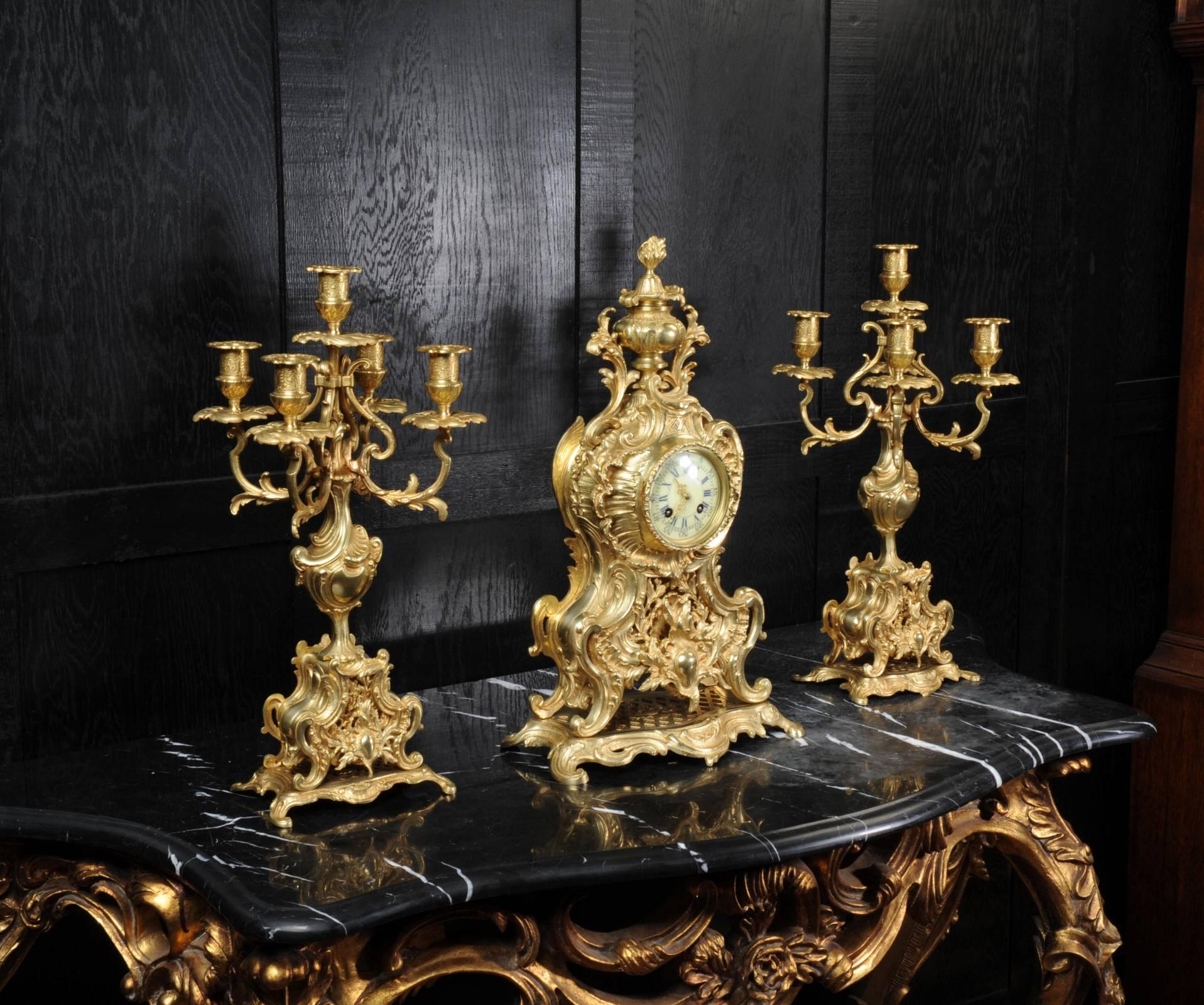 A large and stunning original antique French clock set, beautifully modelled in gilt bronze in the Rococo style. If is profusely decorated with 'C' scrolls and acanthus, the front is fretted to allow a glimpse of the pendulum swinging within.