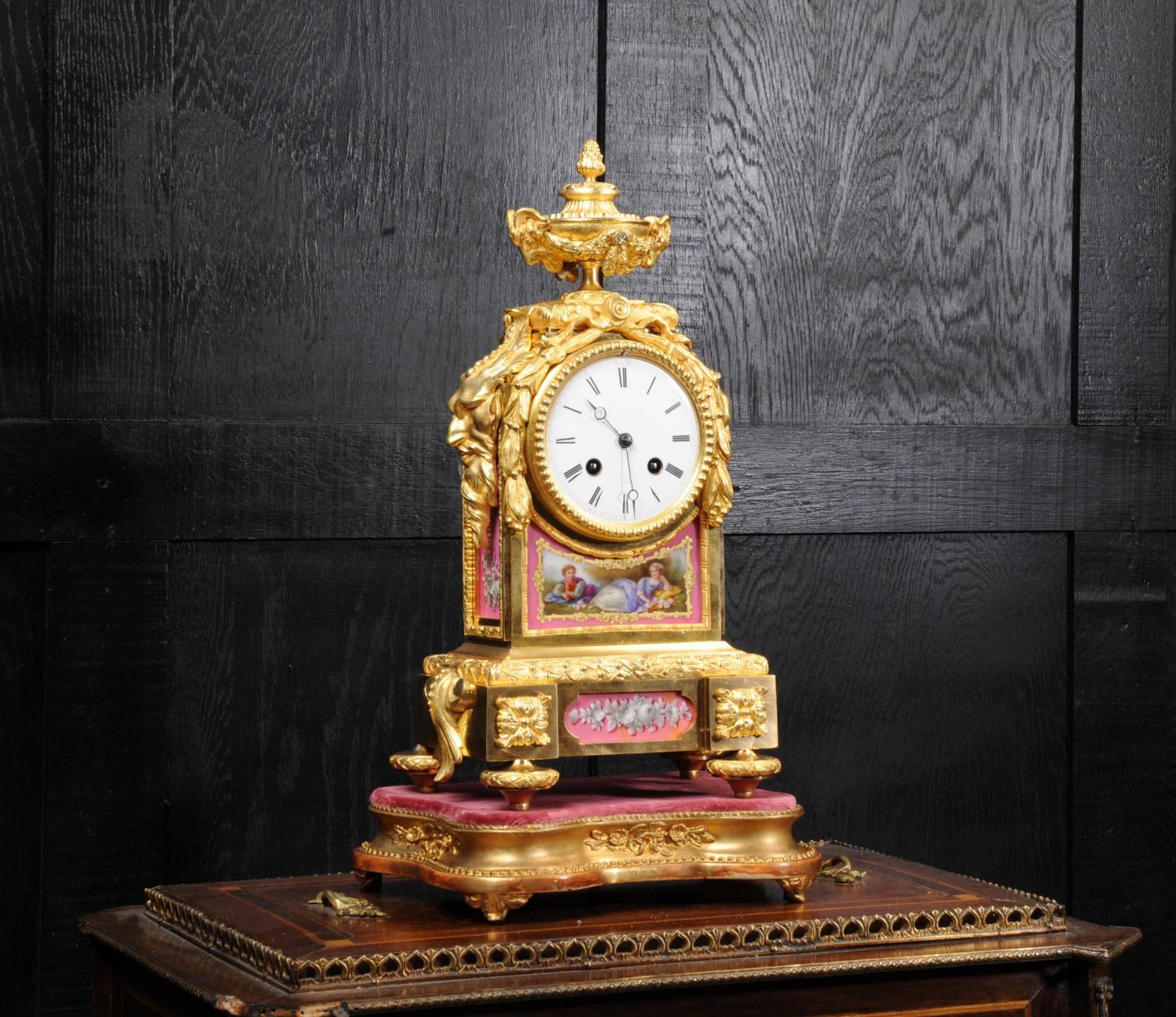A fine and early clock by Raingo Frères Paris. It is beautifully made in ormolu (fire gilded or bronze doré) and mounted with exquisite Sèvres style porcelain with Pompadour Rose ground. The panel below the dial features a charming scene of a couple
