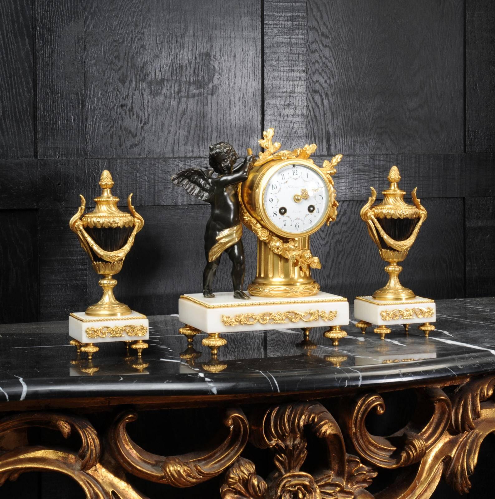 A superb antique French boudoir clock, beautifully made in bronze and ormolu and mounted on white marble bases. It features a bronze cherub draping laurel wreaths over the clock which is mounted on a classical column. Side urns are bronze-mounted