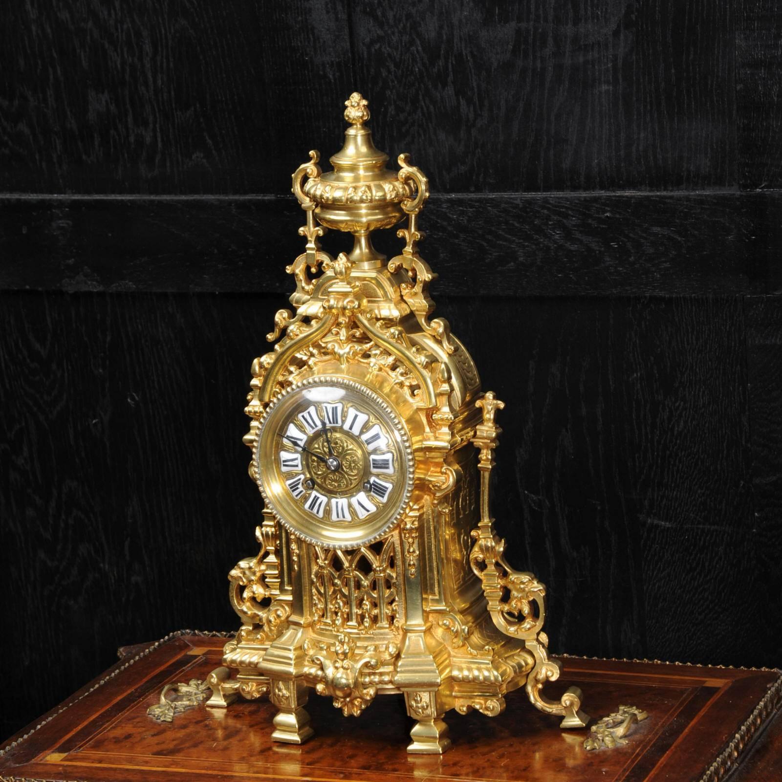 A lovely gilt bronze clock, beautifully modelled in the Baroque style. The front is fretted to lighten the design and allow the pendulum to be seen swinging gently within. The dial is also gilt bronze, mounted with 12 individual porcelain enamel