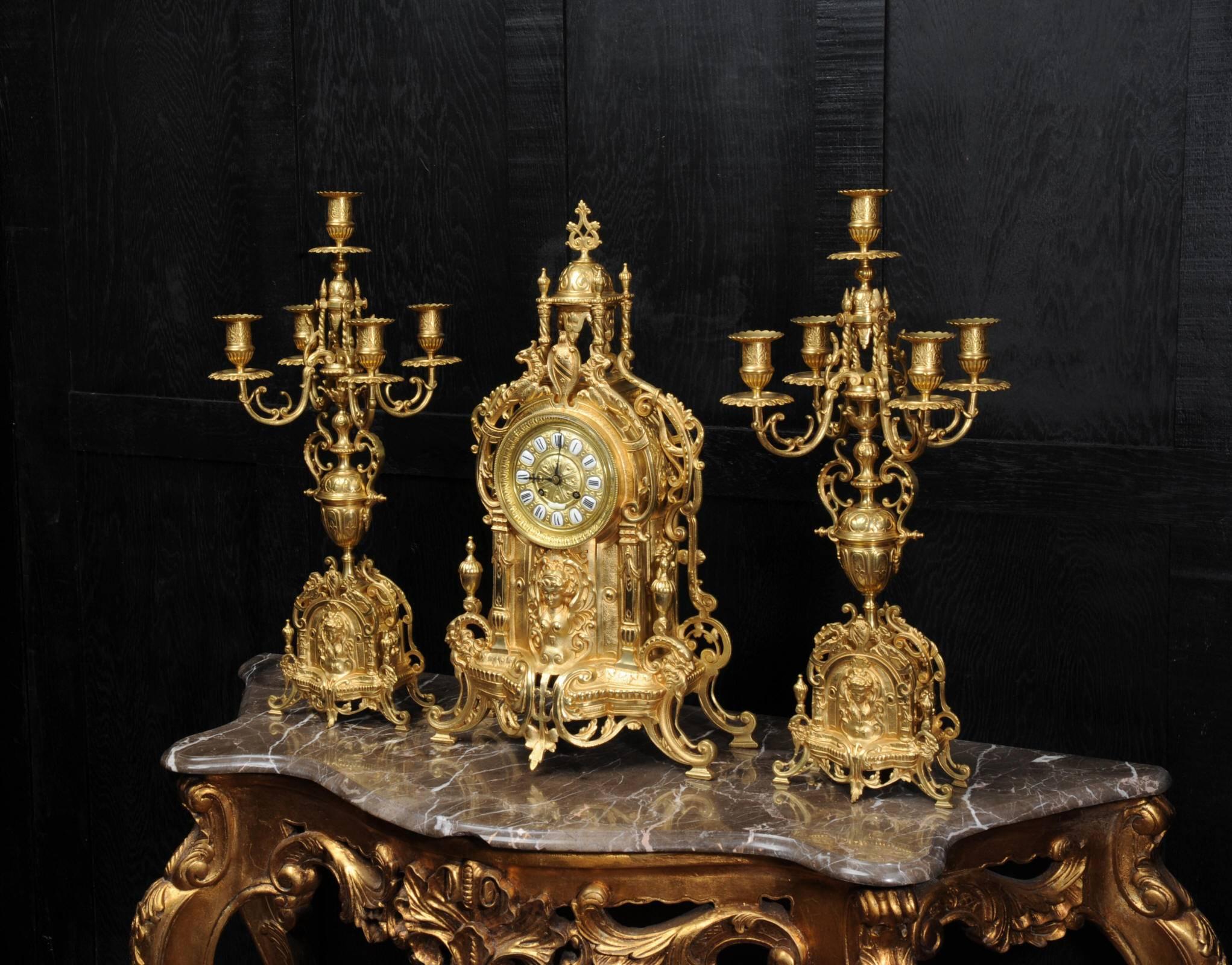 A superb original antique French gilt bronze clock set, circa 1880. It is Baroque in style and features the Goddess Nike in a panel below the dial. Above the dial is a shield with mythical beasts and an elaborate urn standing on four pillars. A