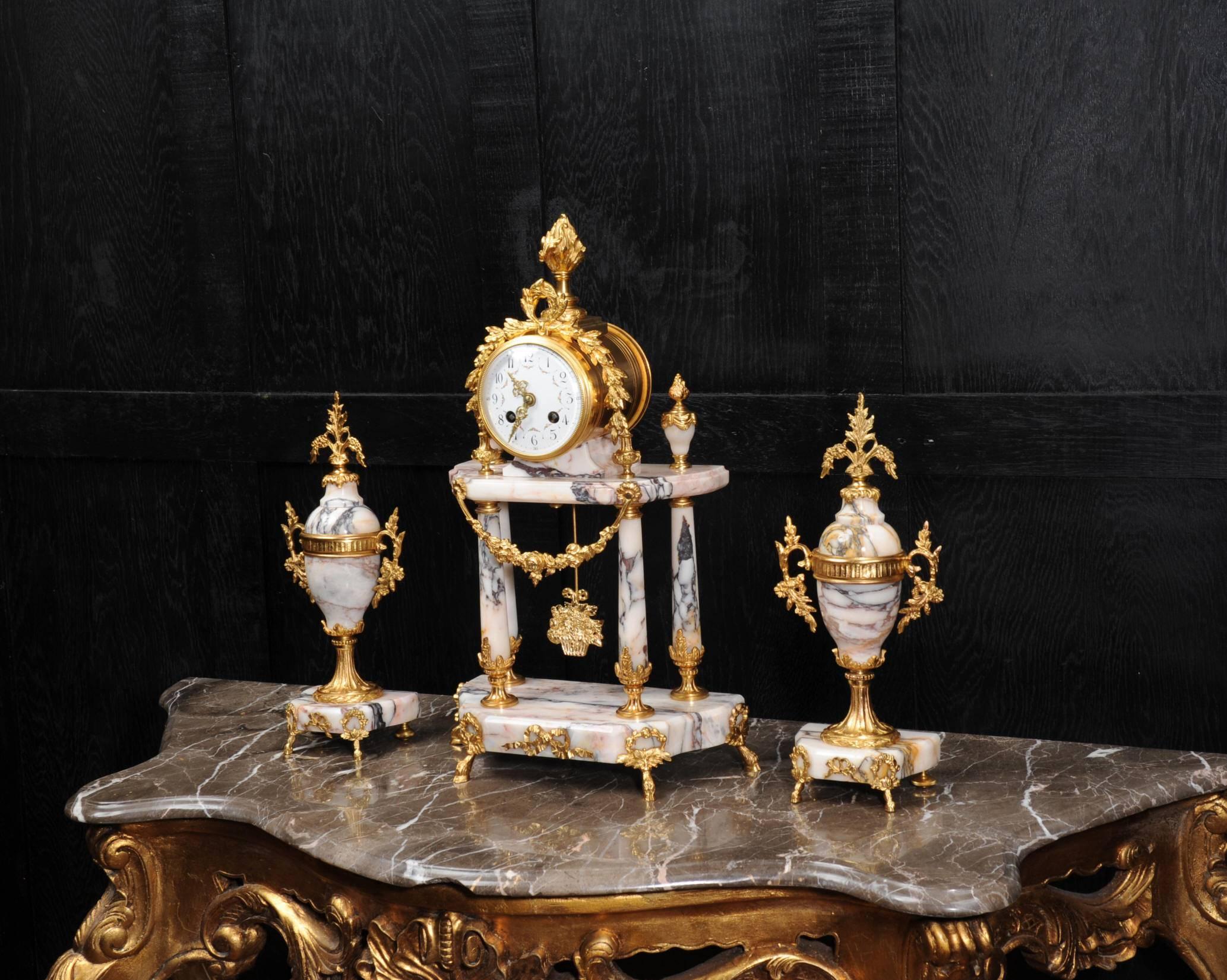 A stunning antique French portico clock set dating from circa 1900. It is made of the most beautiful variegated specimen marble, with salmon pink and silver grey veining, mounted with finely finished ormolu (gilded bronze). It is classical in style,