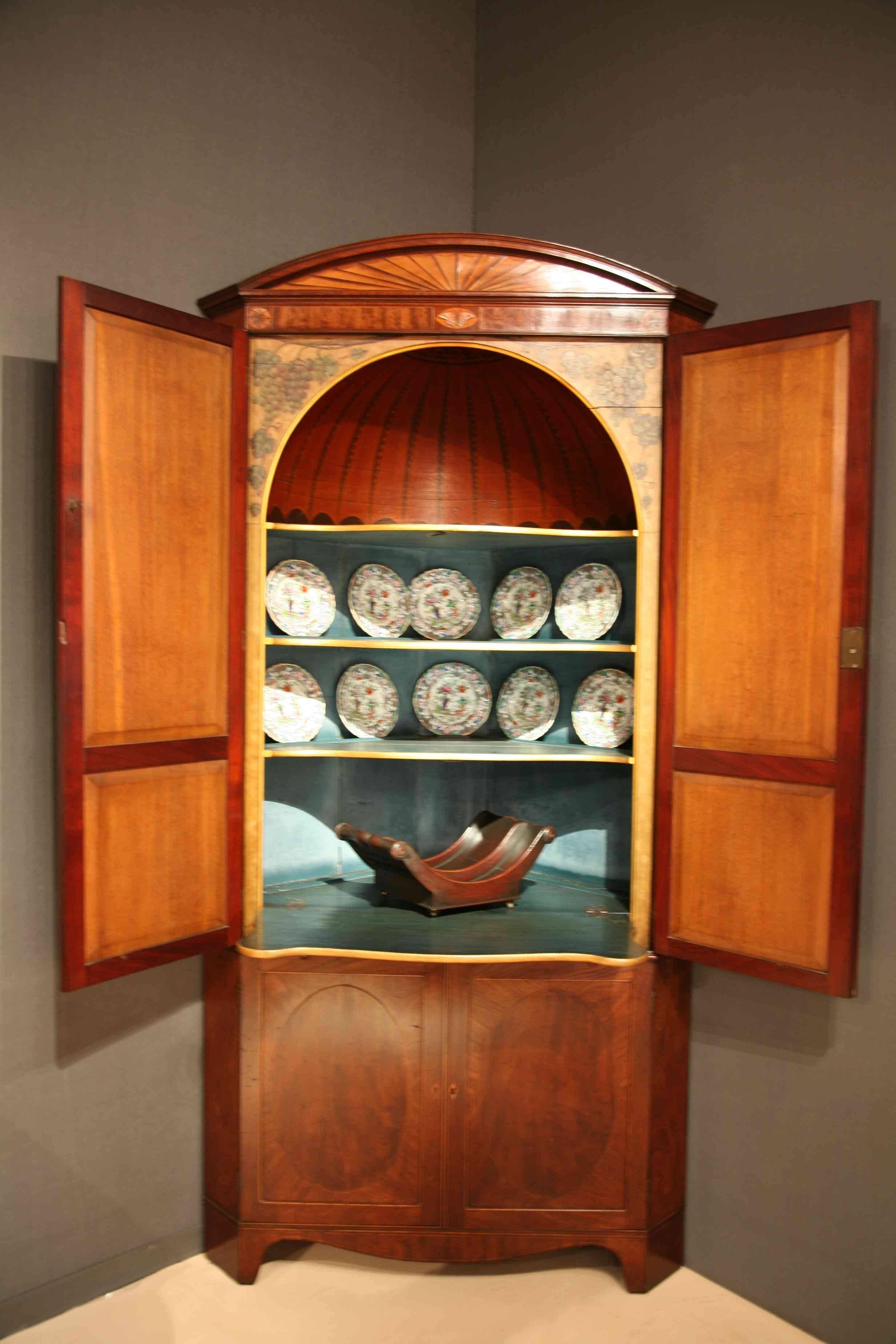 A George III Sheraton mahogany double corner cupboard, profusely inlaid, crossbanded and strung with a decorated umbrella interior,
England, circa 1790.
