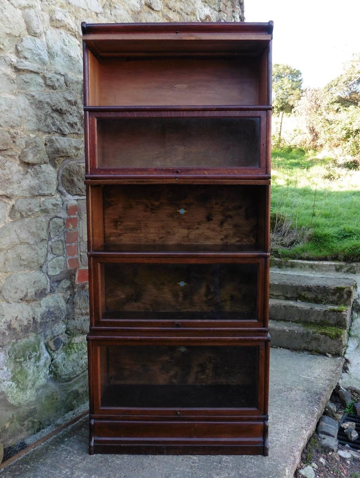 This is a very tall Art Deco bookcase all of the sections have a copper side banding, the five sections of the bookcase are glazed, it has a deeper sections at the base and it stands on a shaped plinth. The bookcase works on the scissor mechanism it