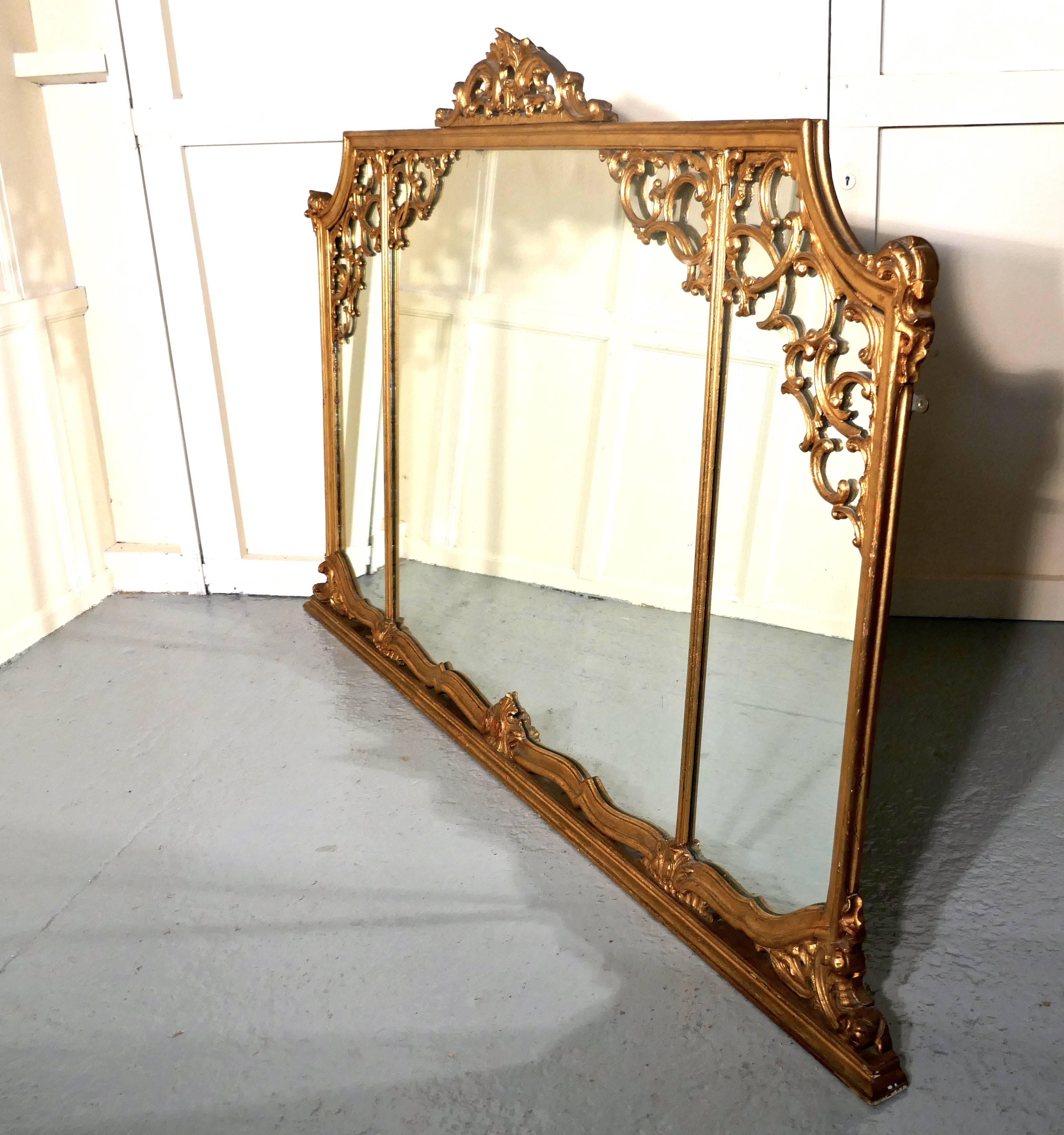 Very large 19th century Adams style gilt over mantel wall mirror

The mirror has a beautiful Rococo gold frame with three mirrors, at the top it is elaborately decorated with carved swags of leaves and Ribbons and a crest at the centre. The base