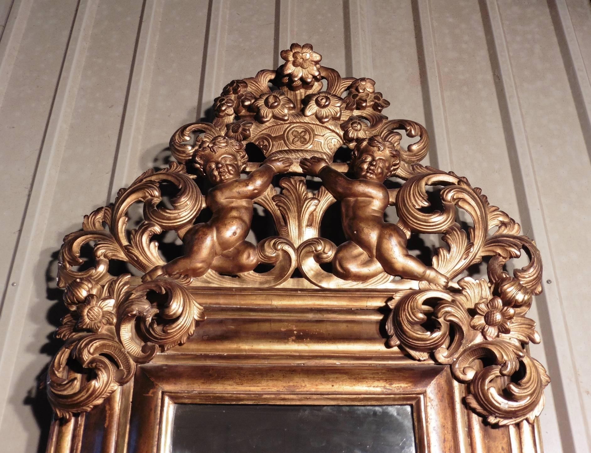 This is the most impressive mirror, a charming piece, dating from 1780.
The glass is set in a deep moulded frame which is crowned with cherubs holding a basket of flowers, the flower theme is repeated at the upper corners and the centre bottom of