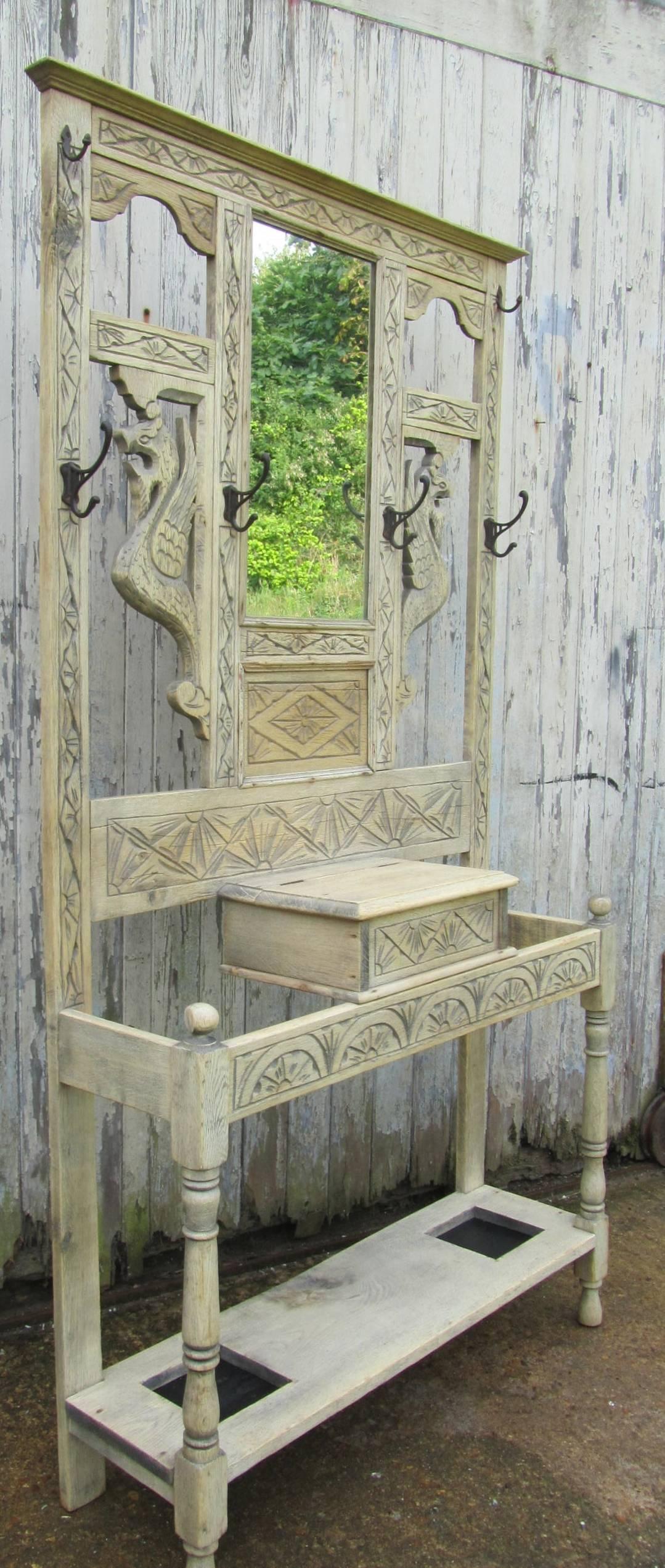 This is a handsome piece, it is carved oak, which has been stripped of its dark color and given a new bleached look. The stand has with six Iron coat hooks, there is a mirror in the centre flanked by carvings of mythical dragons. The lower section