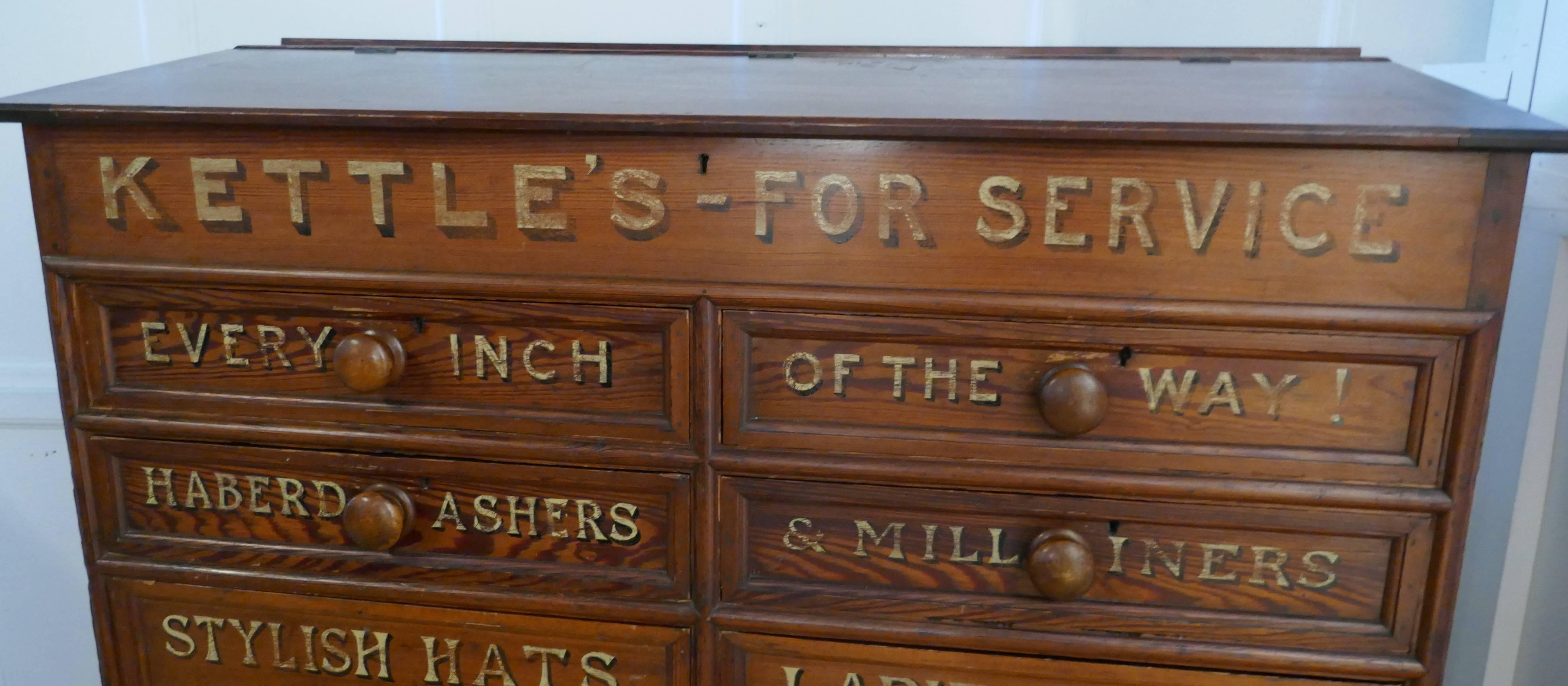 This is a large chest of drawers, it has eight drawers, of varying sizes below a sloping cashiers desk.
The cabinet is made in solid pitch pine it is a very heavy piece. 
The front of the chest has been painted for Kettles Store, with information