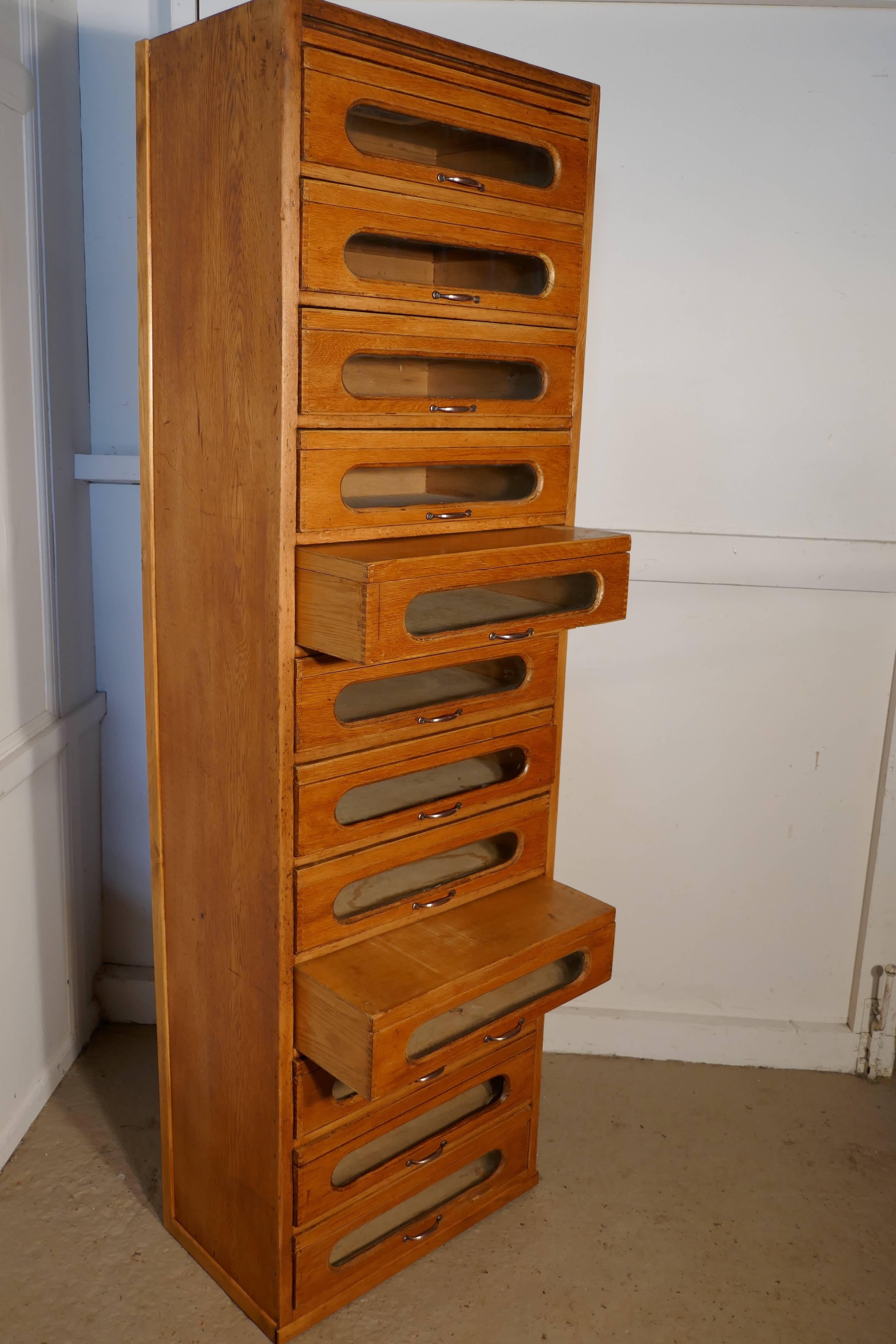 This tall box drawer haberdashery cabinet has unusual lidded drawers, the cabinet has 12 glass fronted drawers, all with wooden lids and copper handles. The cabinet is made in golden oak a piece like this is ideal for any stylish shop interior or