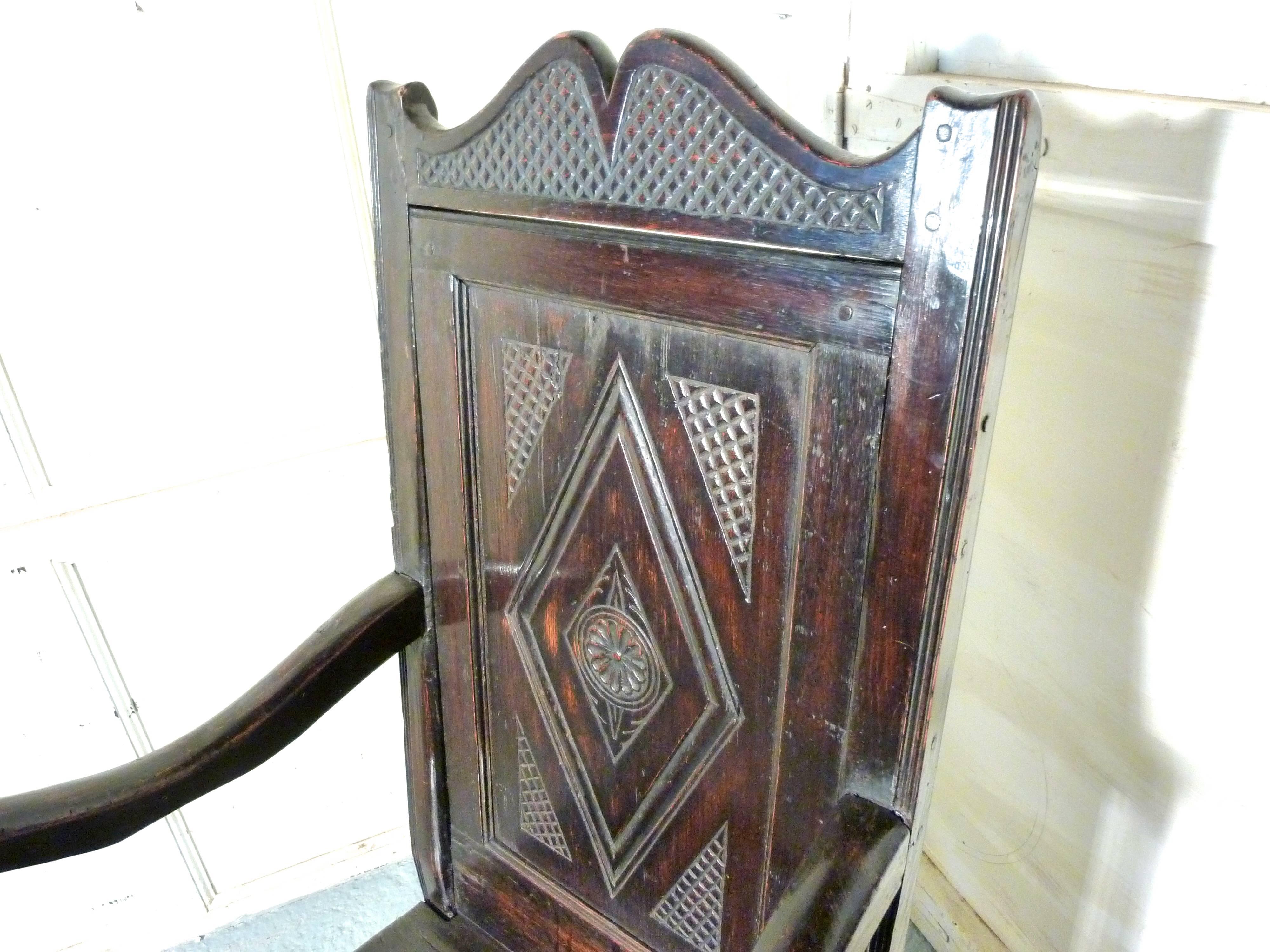 This handsome chair, has a magnificent patina, it is somewhat dark in colour, the solid plank seat has a little carving to the front border, the back is carved with a large geometric design and a shaped top rail. The sturdy shepherds crook arms are