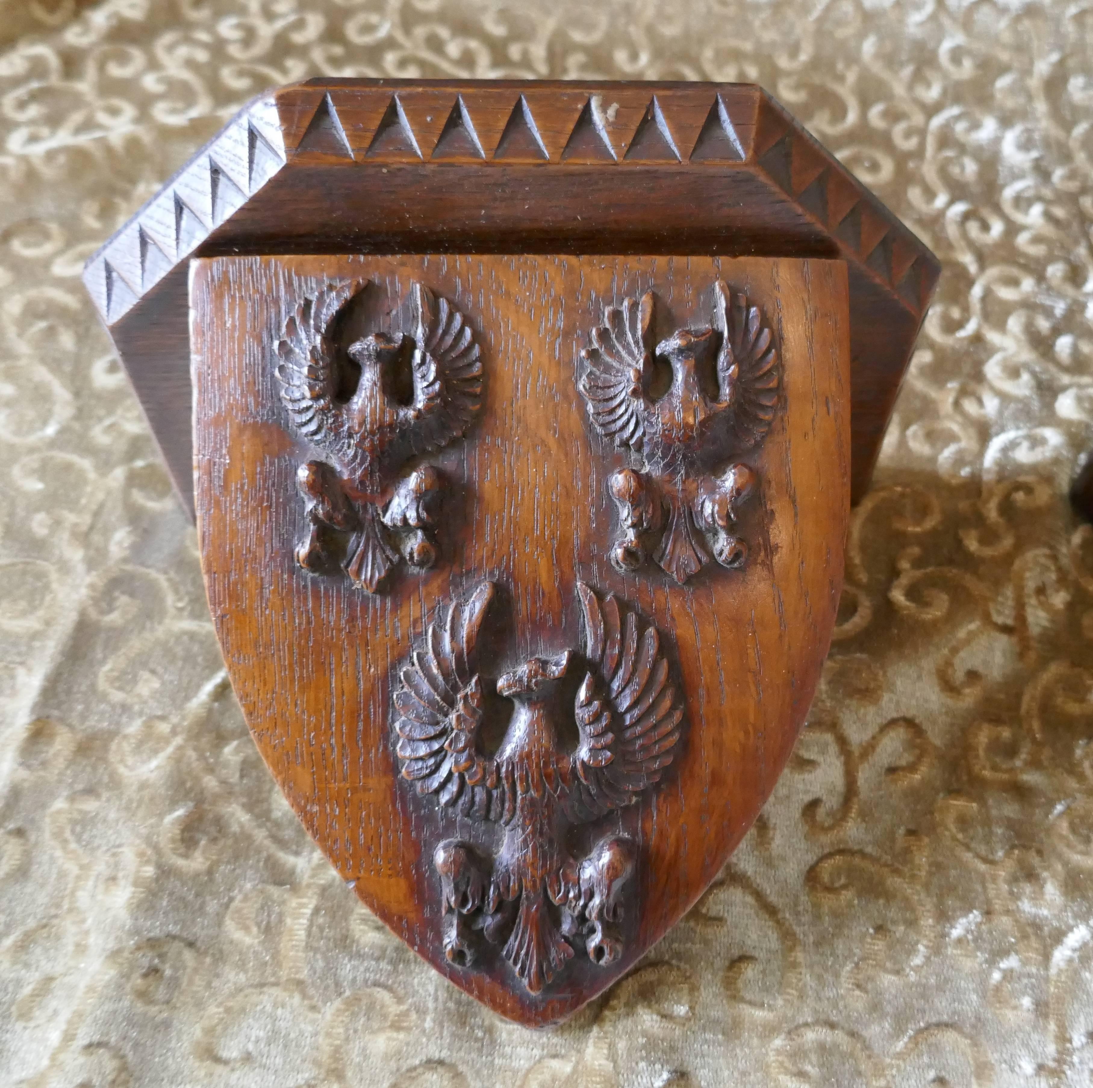 A pair of 19th century carved oak wall brackets, armorial crests

This is an exquisite pair of Arts and Crafts carved wooden wall brackets they have carved shields, one with three phoenix the other with an open book enclosed by coronets, the Latin