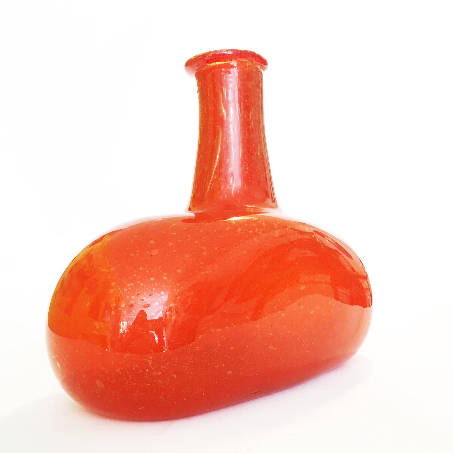 Big studioglass-vase from the 1960s. The vase is mouth blown and consists of thick orange colored glass with tiny bubbles and golden particles. The bottle shape is slightly amorph, which gives the piece a special touch. The vase is unsigned.