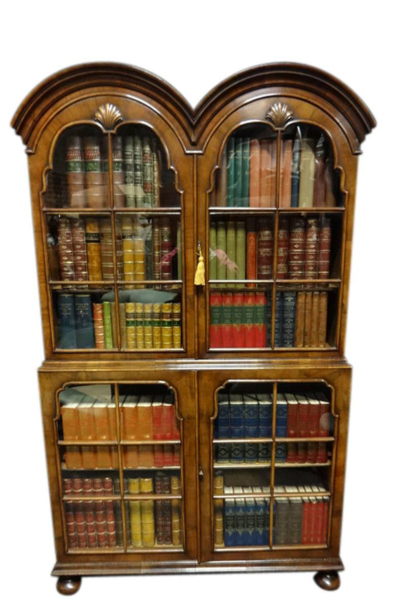 A top quality double walnut bookcase with double domed top, end grain astral grazing bars and shelf edging, fixed shelf to the lower section and two adjustable shelves to the top, standing on turned walnut bun feet, in excellent original