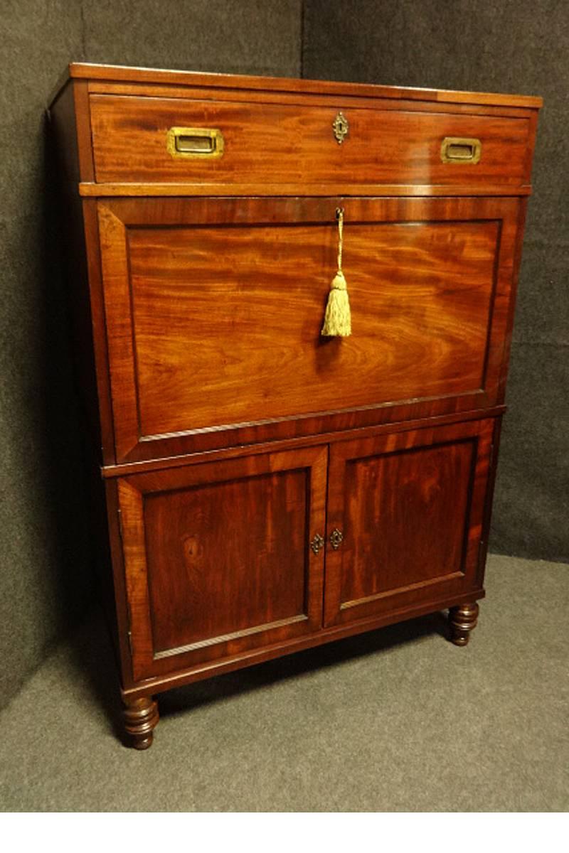A superb Mahogany Campaign secretaire single drawer above a secretaire desk with pigeon holes, under two cupboard doors open to reveal three drawers all with inset brass handles, screw in brass bound turned mahogany feet, brass escutions added