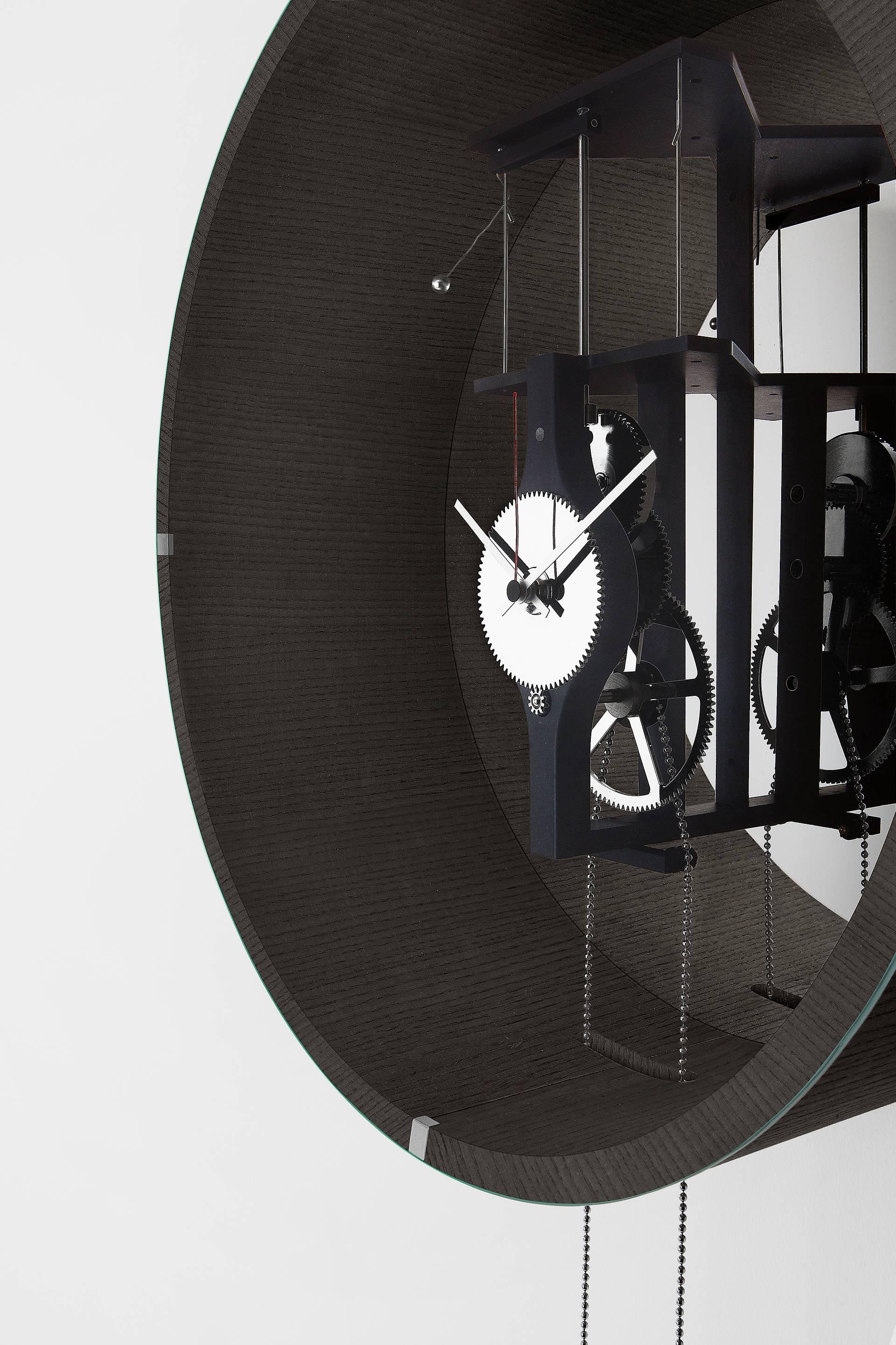 Manual winding pendulum clock. Tobacco stained ash structure and 6 mm extra light transparent tempered bevelled front glass.
“Supermirror” bright stainless steel back.
Black anodised aluminium and chromed brass mechanism.
Striking mechanism clock.
