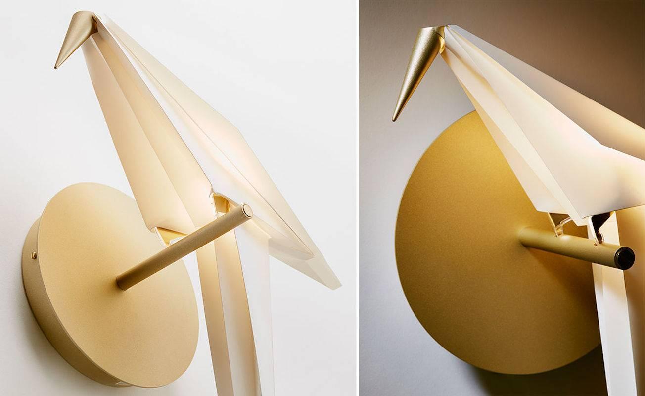 Moooi Perch LED wall sconce light in brass with small white bird. 

A bird is gracefully balanced on a tall metal perch, beautiful and proud, a swinging glimmer of warm light, yet you are inside, after daylight has faded, under the spell of the
