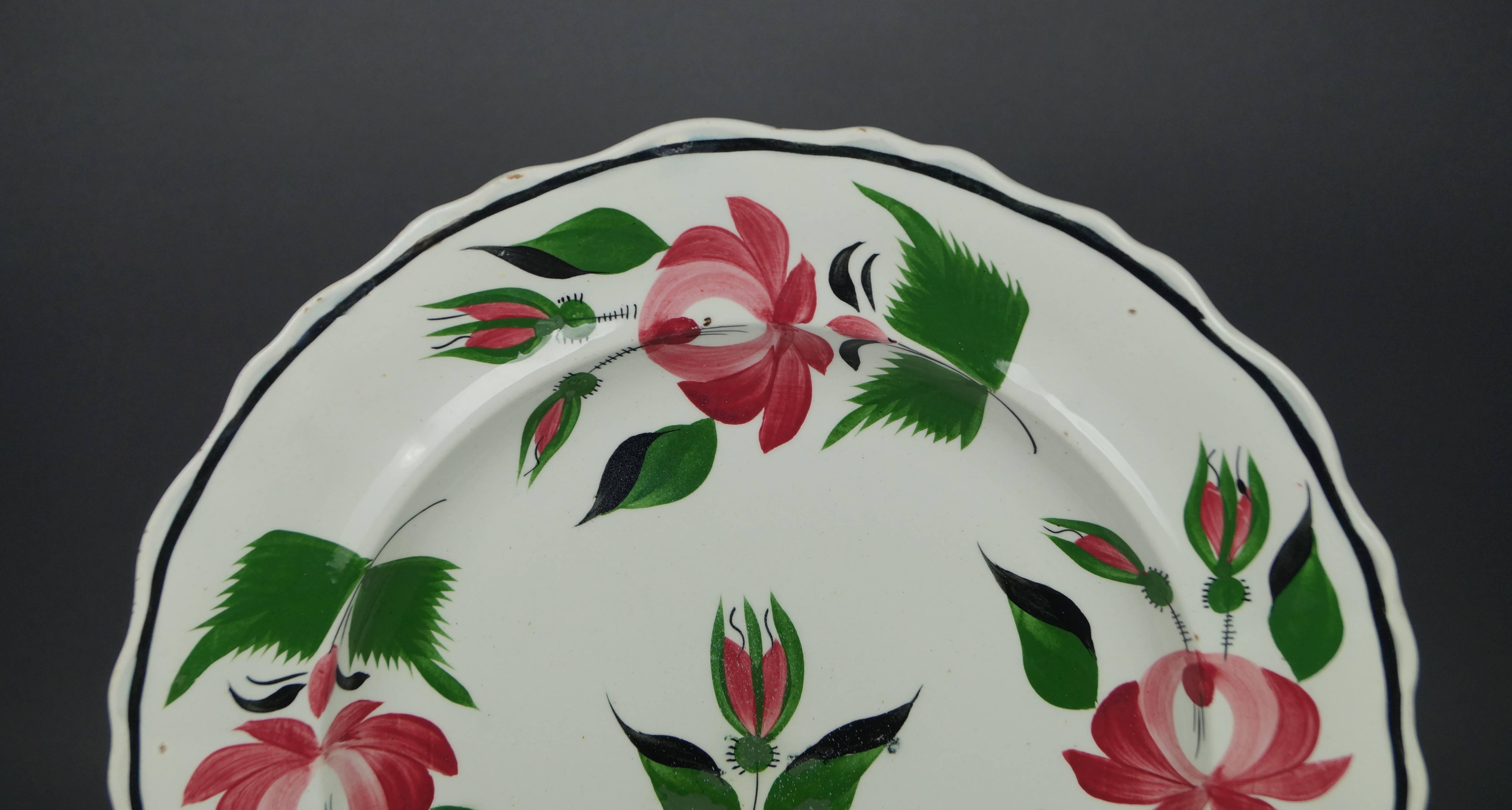 This traditional English creamware plate was produced in the early 19th century. It was produced in Staffordshire, England by William Adams circa 1815. The hand-painted Rose pattern features vibrant pink, green and unusual black decoration to the