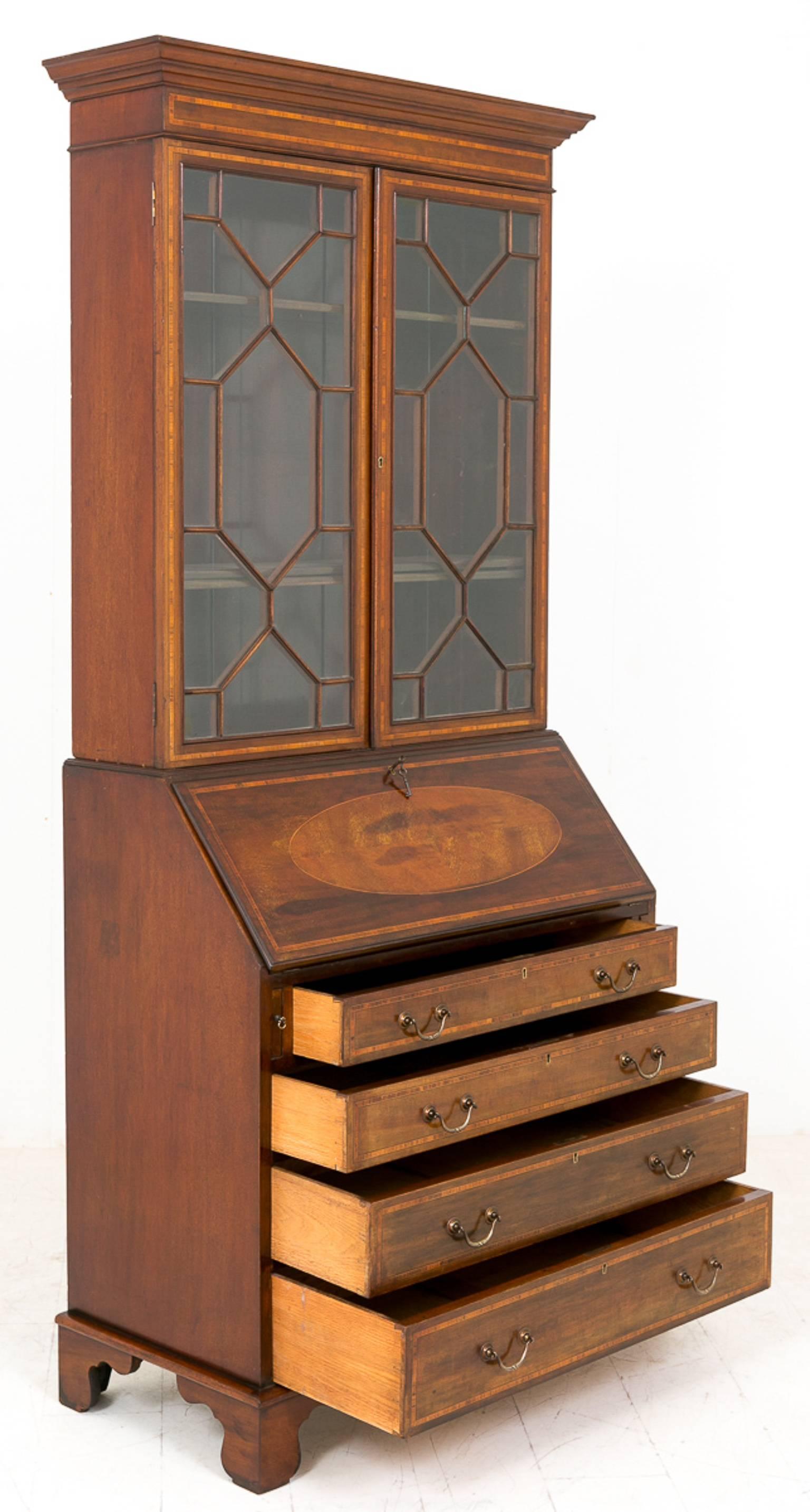 Sheraton Revival mahogany bureau bookcase.
Featuring bracket feet.
Four oak lined drawers with original brass handles.
The fall with an oval inlay opening to reveal an arrangement of drawers, pigeon holes and a central door.
Behind the astragal