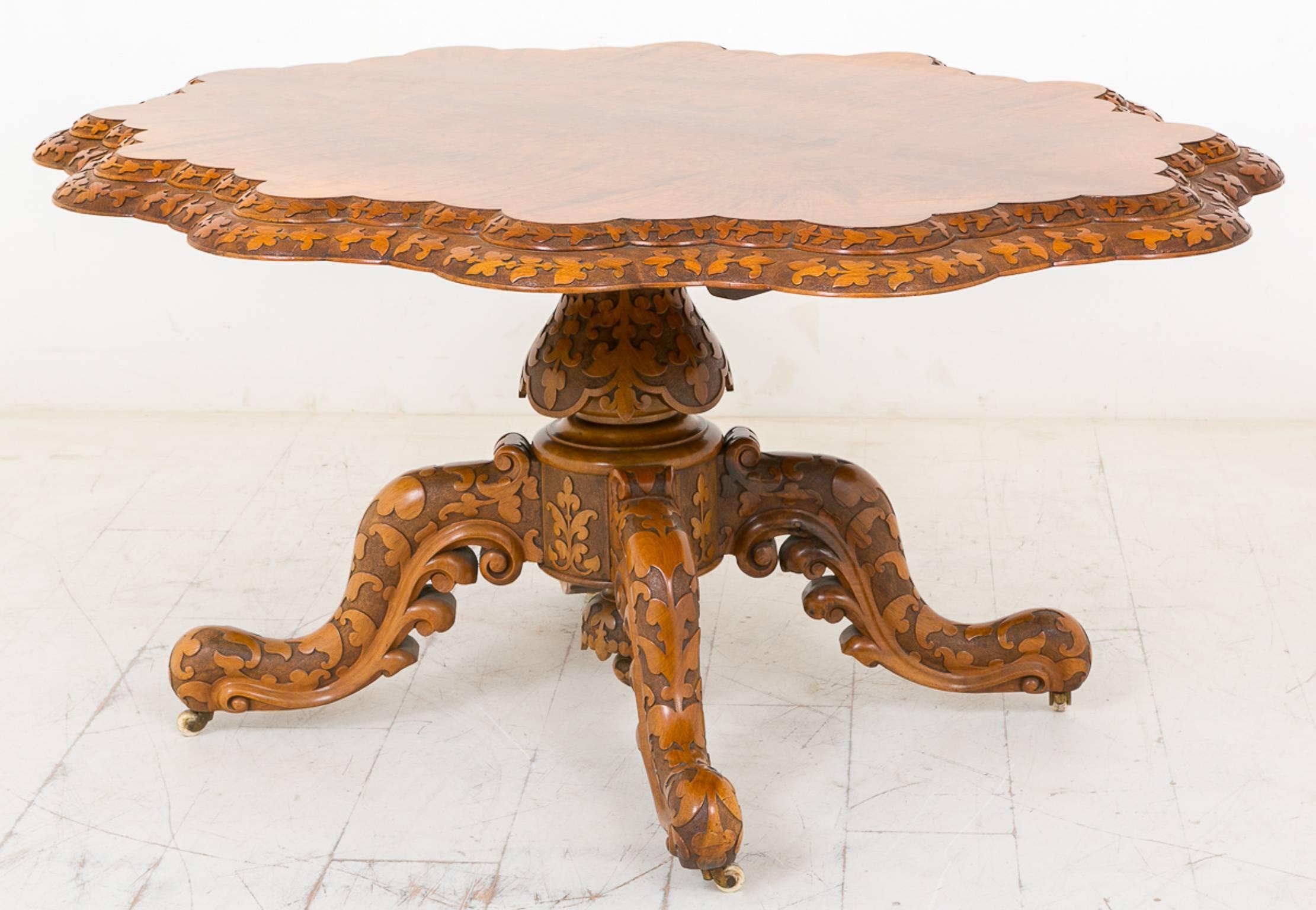 Superb quality walnut centre table, standing on a heavily carved quatrefoil base with original porcelain castors.
The supporting column also heavily carved.
The burr walnut shaped top featuring carved double mouldings. This table tips for easy