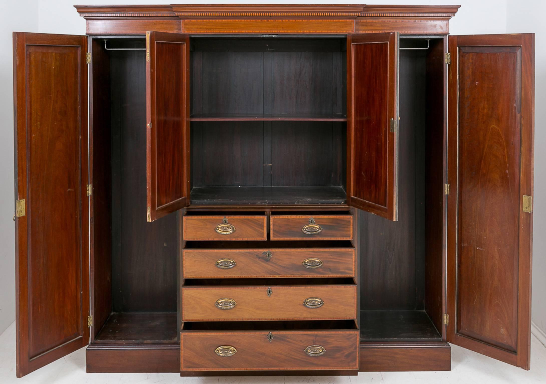 Sheraton Revival mahogany breakfront wardrobe standing on a plinth base.
The centre section having a two over three chest and a two-door cupboard above, flanked by full length hanging spaces.
Original locks and handles.
This piece is inlaid with