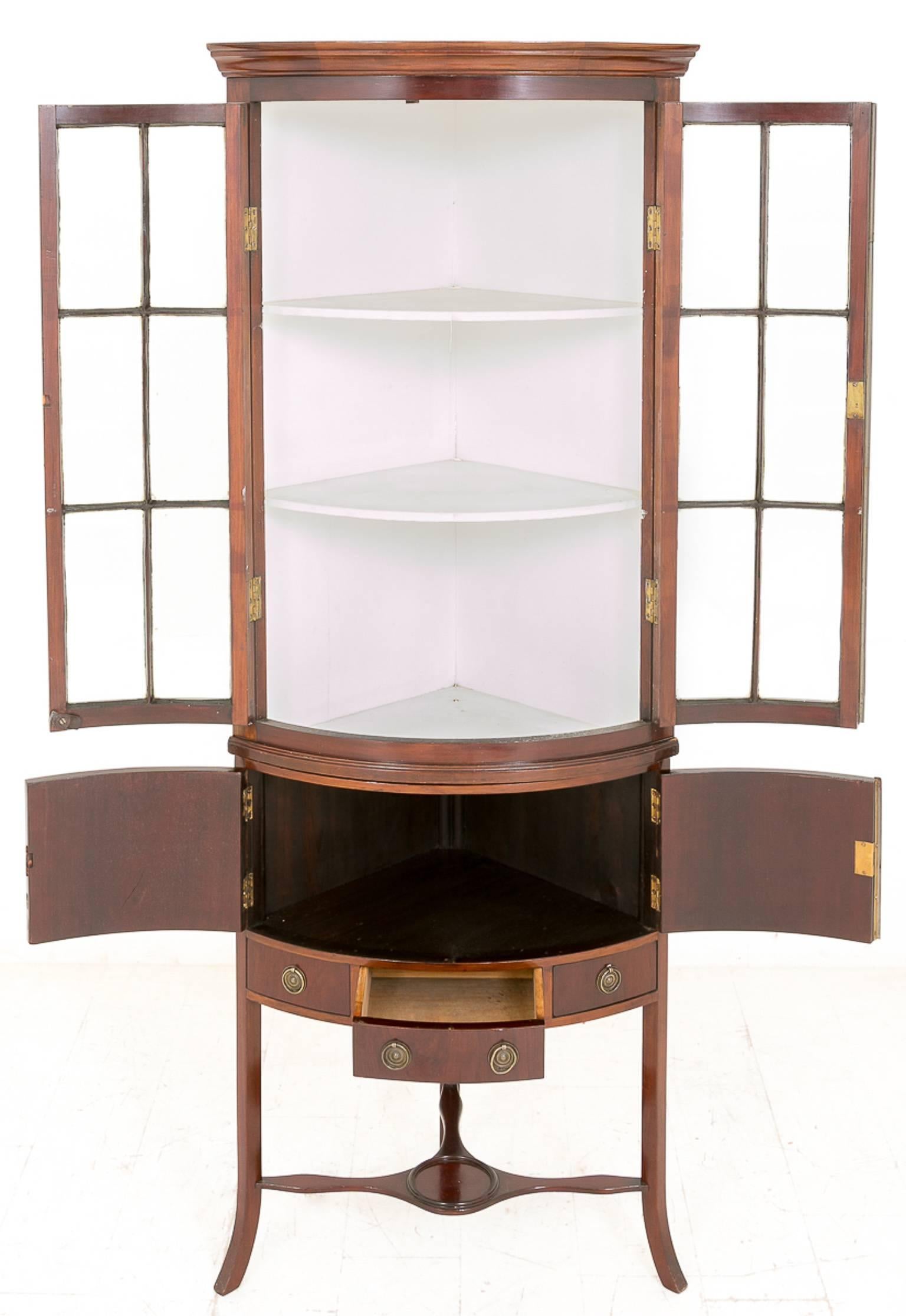 An elegant mahogany bow fronted corner cabinet. Standing on a swept leg with a tri form stretcher.
Featuring one central drawer and one blind two door cupboard.
The top section having two glazed doors.

Size:
Height 75