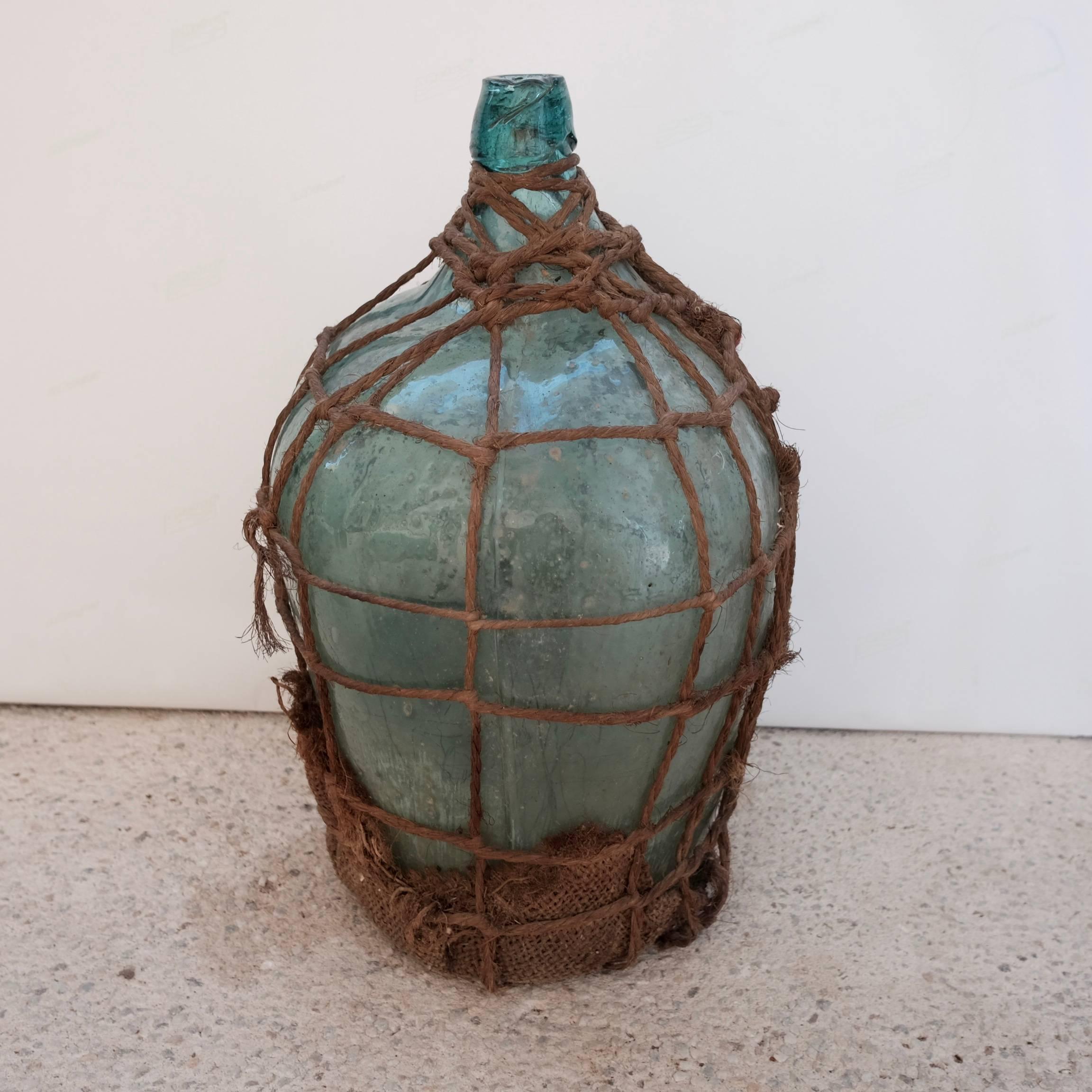 This vintage, rustic bottle comes with a unique wrap woven using ixtle rope (agave fiber). Color of glass is a medium toned blue or green. The spout is rustic and completely irregular. A slight bit of dirt remains intact throughout the jug which can