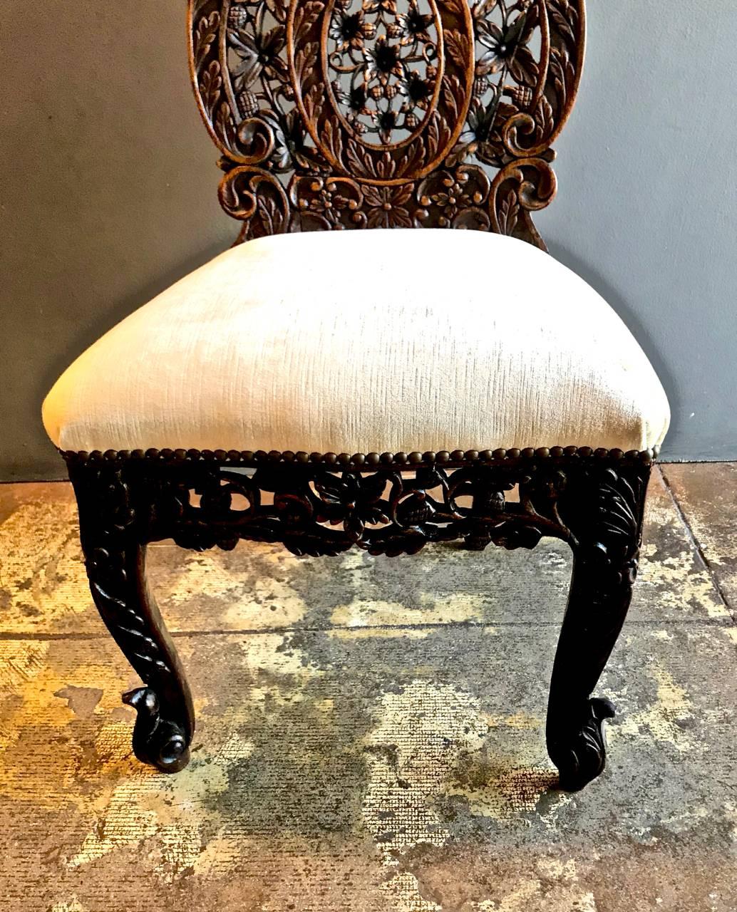 This is a intricately carved sculptural rosewood Anglo-Indian side chair that has been newly upholstered in a very light gold-toned Italian silk velvet. The chairs is in good condition with a couple of very old minor restorations. The carving is all