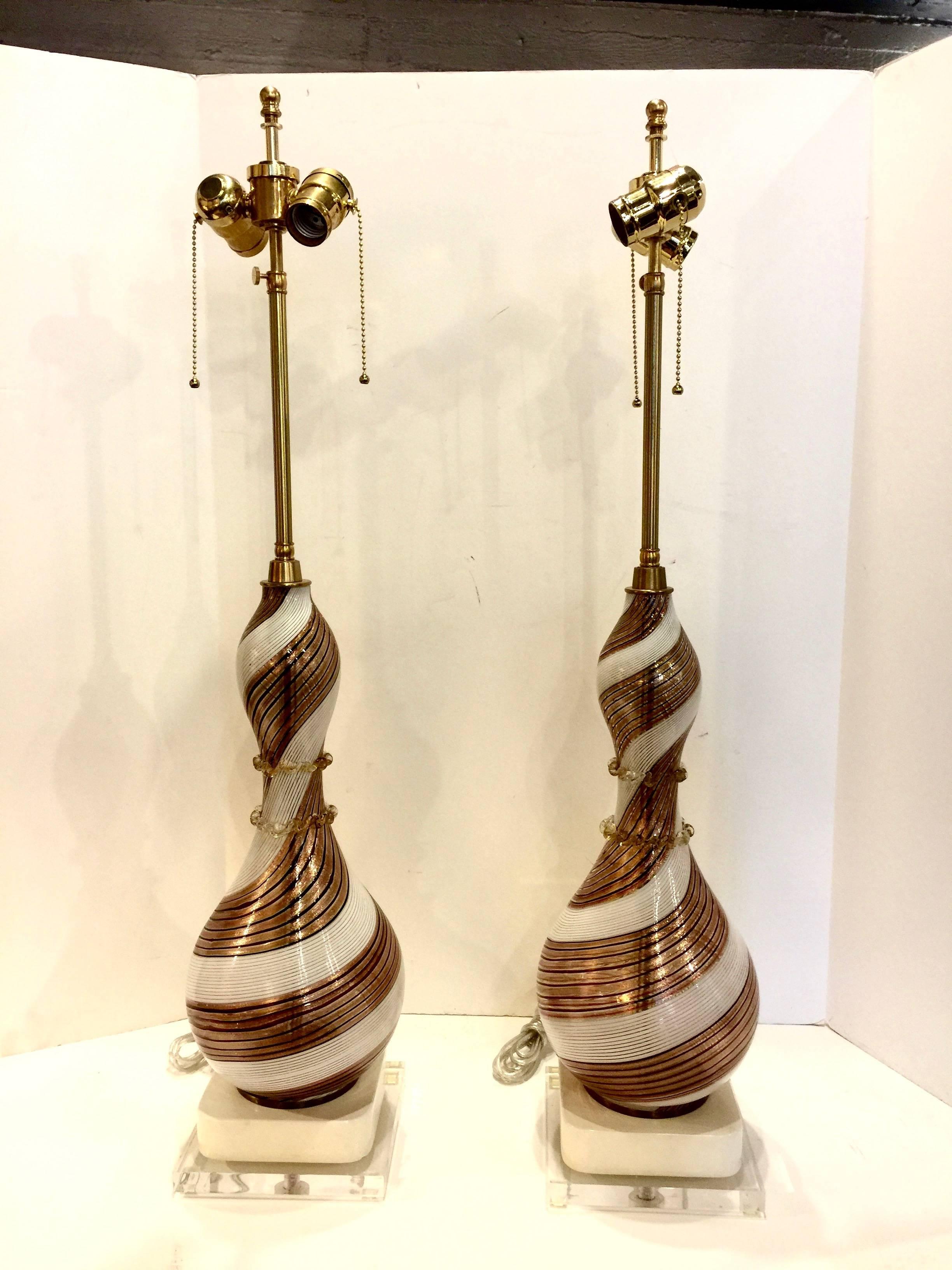This is a stunning pair of swirled mouth blown Murano glass lamps by the famous Dino Martens. The glass bases were created with swirled and ribbed gold accented glass with white opaescent glass forming the contrasting swirl. New Lucite bases, top