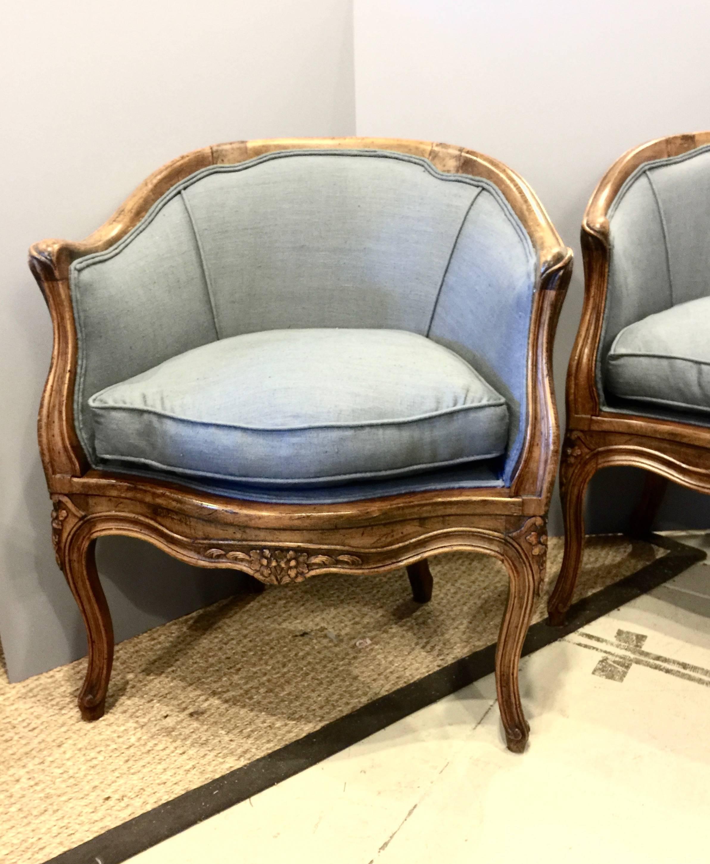 This is a great pair of Louis XV-style walnut barrel back bergeres. These chairs date to the first half of the 20th century and are in excellent overall condition having been newly upholstered in a French blue/grey 100% linen fabric. The carved