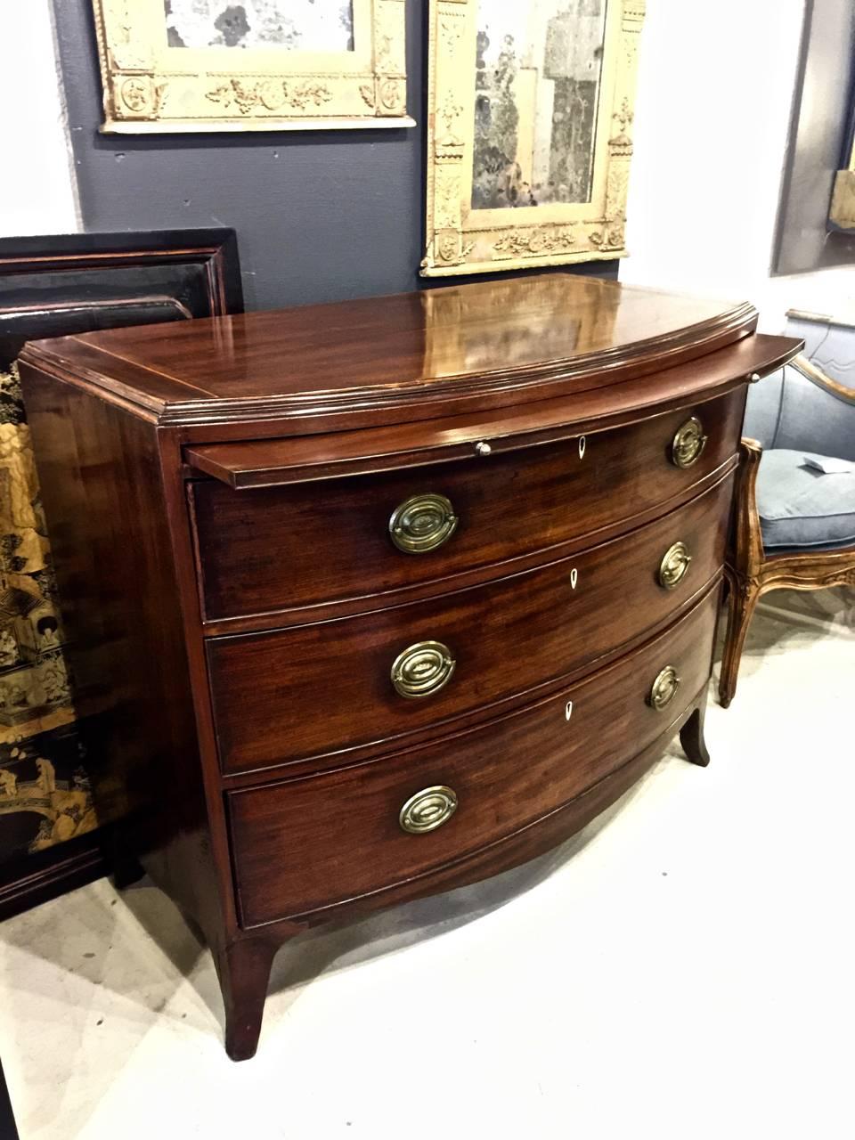 This a great beefy late 18th-early 19th century. George III bow front chest of drawers with brushing slide. The chest, although large, has elegant proportions, French feet, a brushing slide, good figured mahogany, ivory escutcheons and original