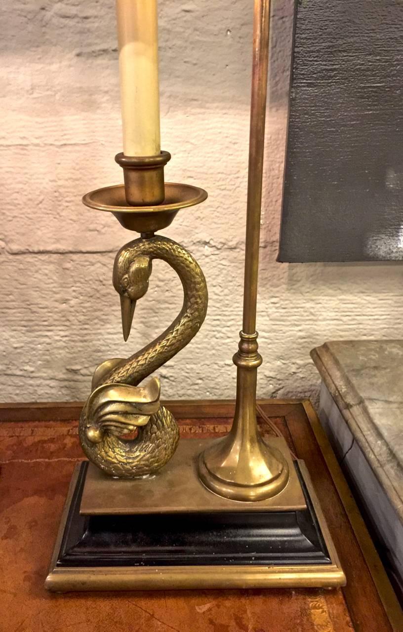 This is an iconic pair of Chapman solid brass and tole neoclassic form lamps. The lamps are in the Napoleonic Empire style and feature cast swans supporting candlestick sockets surmounted by a black tole shade, the lamps are finely detailed, as