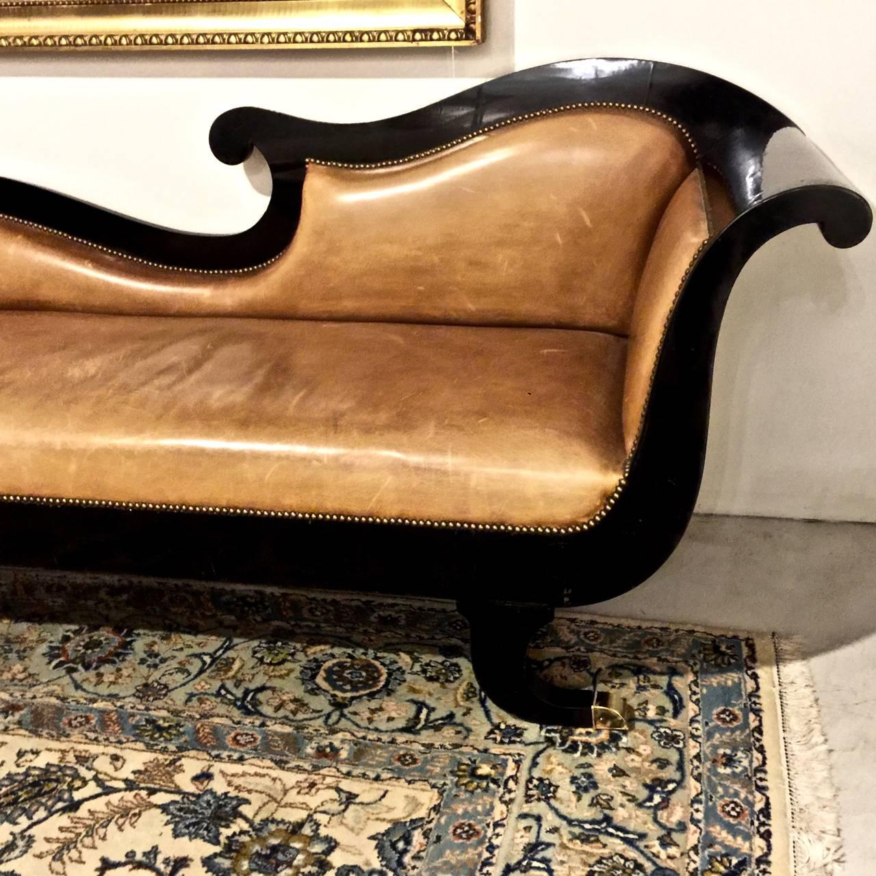 This is a highly decorative English Regency lacquered sofa that dates to circa 1825.
The sofa is upholstered in top quality pale caramel-toned leather that has acquired just the right amount of patina. The back silhouette is very graphic making the