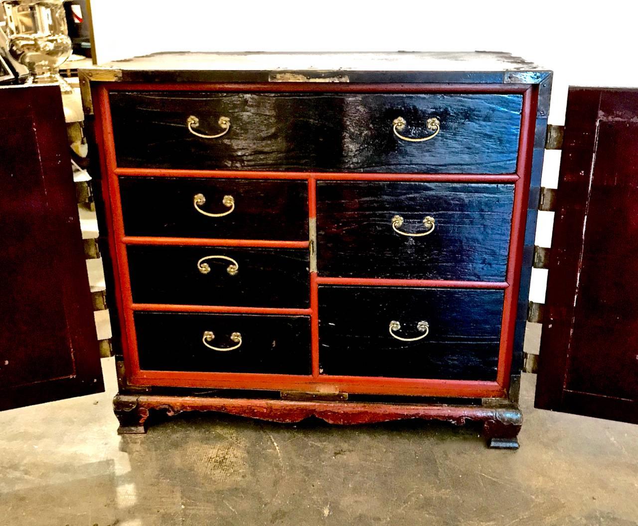 This is a wonderful multi-purpose Korean small chest on stand that features six drawers concealed behind a pair of figured wood carved doors that are finely detailed with hand chased brass mountings and lock plate. The exterior of chest is lacquered