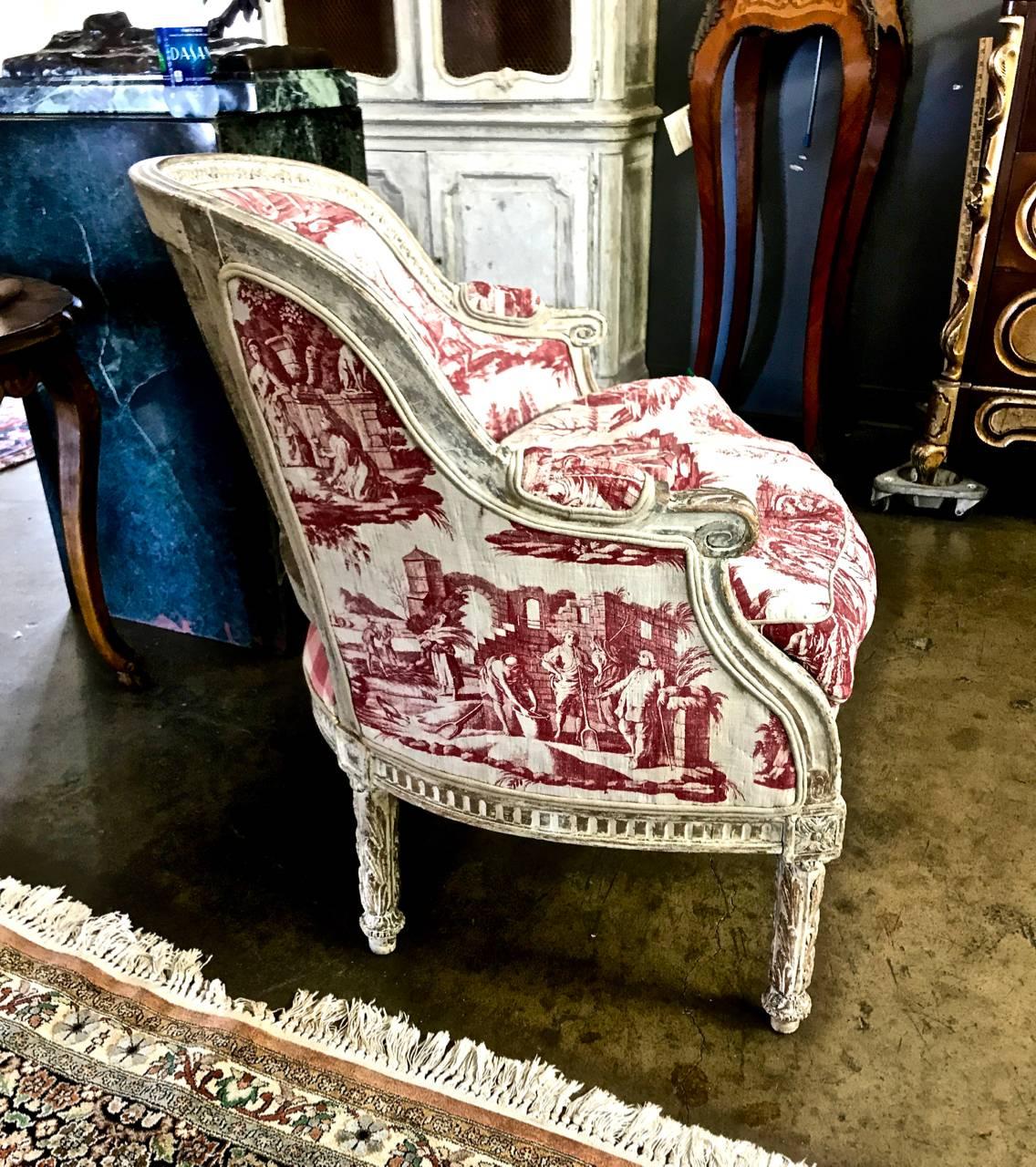 This is a stunning example of a painted period 18th century, Louis XVI bergere. The bergere appears to retain its original off-white/ivory finish and exhibits great natural patina. It has been upholstered in an early 19th century Toile that features