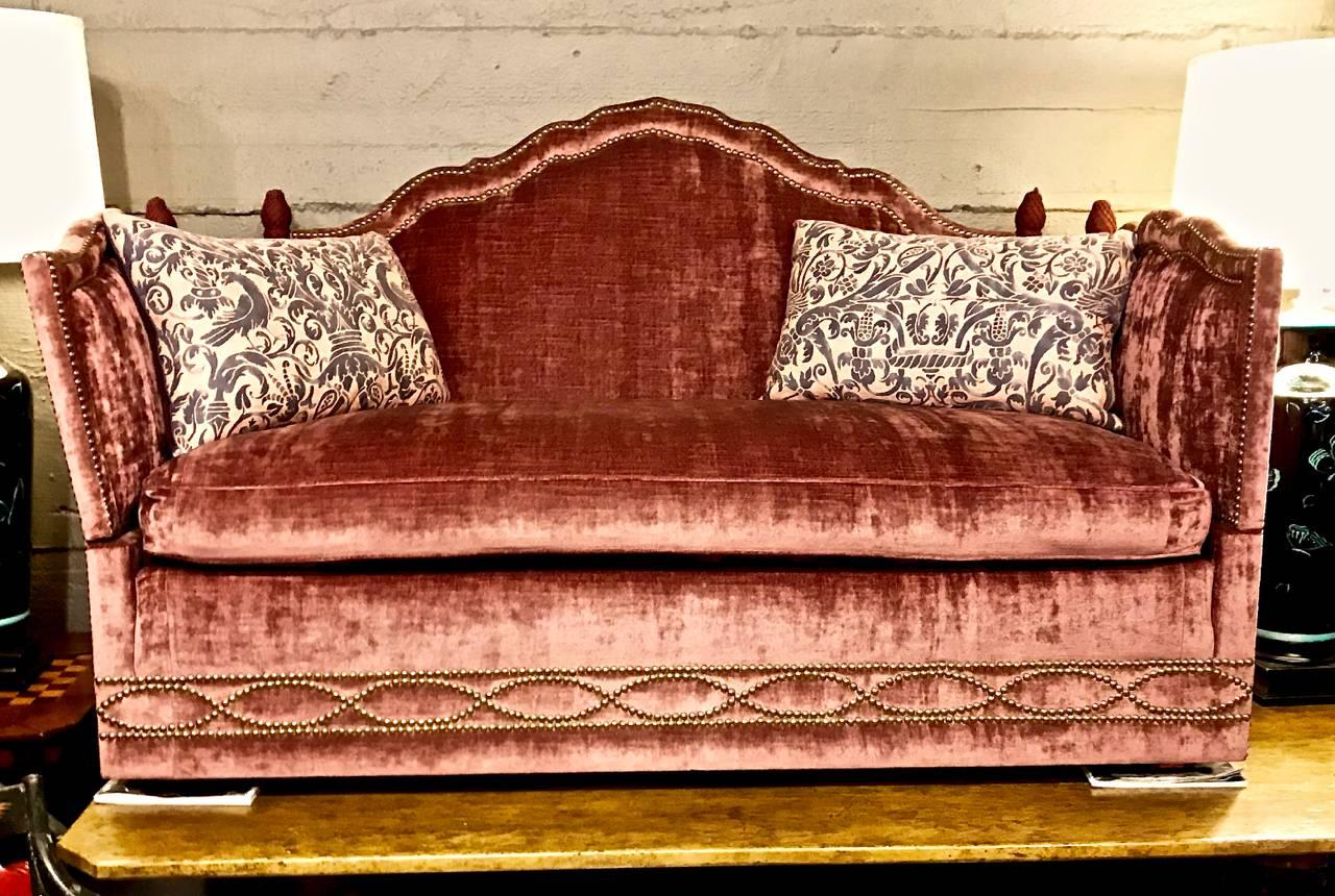 This is an all original Knole style sofa by Baker. The sofa is beautifully upholstered in a mauve, tending to violet, silk and cotton velvet which is detailed in a brass nail head outline with additional nail head ornamentation. The sofa is in