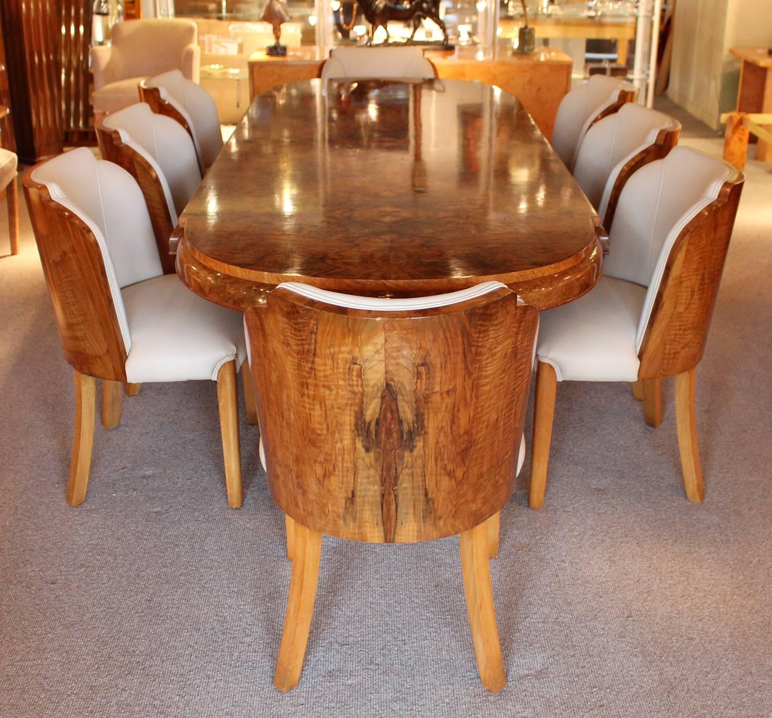 An Art Deco dining suite with eight cloud back, walnut wrapped chairs upholstered in cream leather. Figured walnut table set over two pedestals with shaped feet. By Harry and Lou Epstein.

Measures: Table H 76cm, L 245cm, W 100cm

Chairs H 82cm, W
