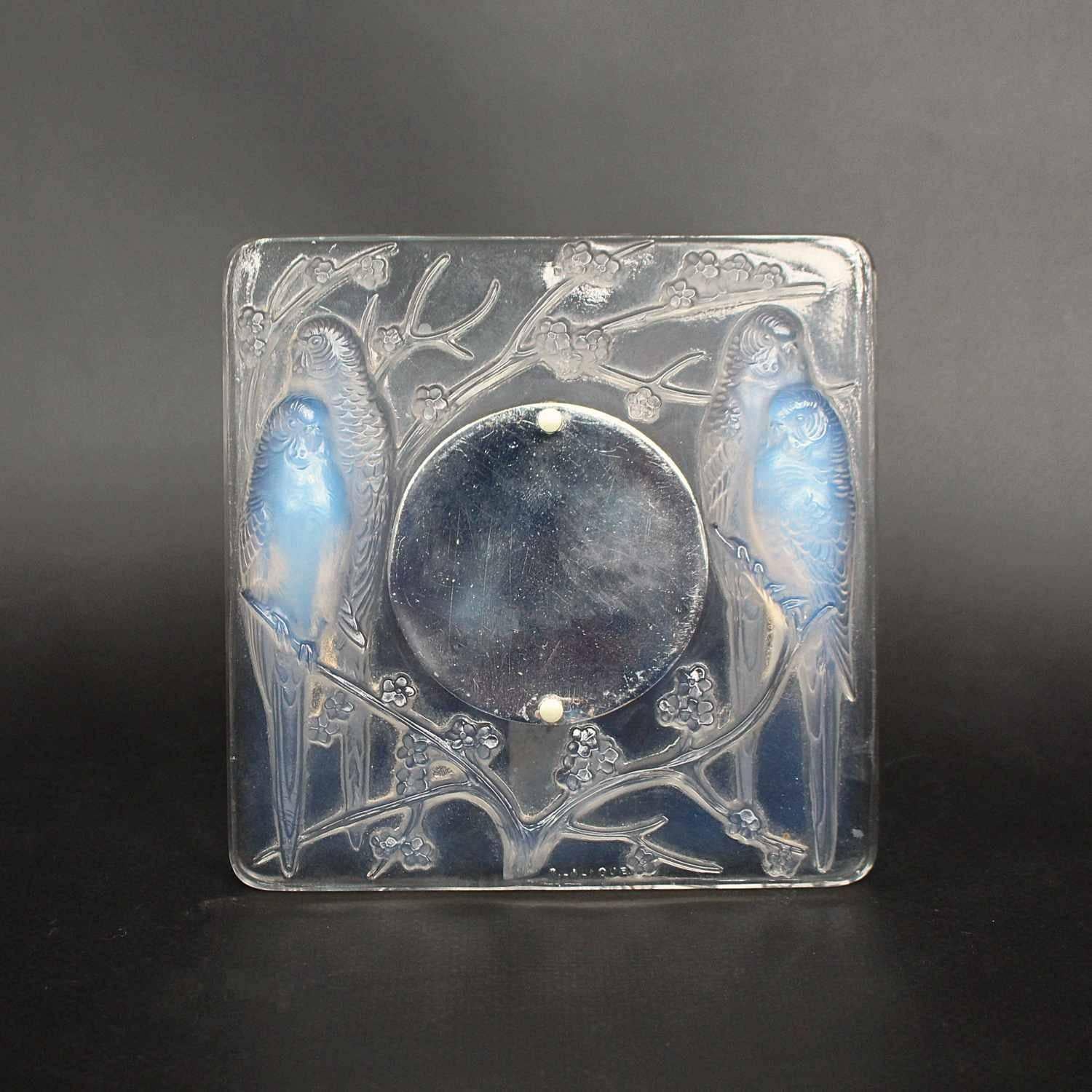 Inseparables, an Art Deco frame by René Lalique (1860-1945) – also known as ‘Quatre Perruches’. In press-molded, clear and opalescent glass. Raised motif of four lovebirds perched among branches of prunus blossom. With circular metal plate and arm