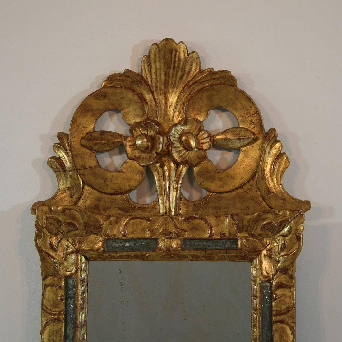 An extremely rare Louis XIV period mirror with stunning gilt. The frame is hand-carved with stylized fleurs-de-lys & foliage, and the margin is pierced with eight narrow rectangles of mercury glass plate. On top, the beautiful pierced crest features