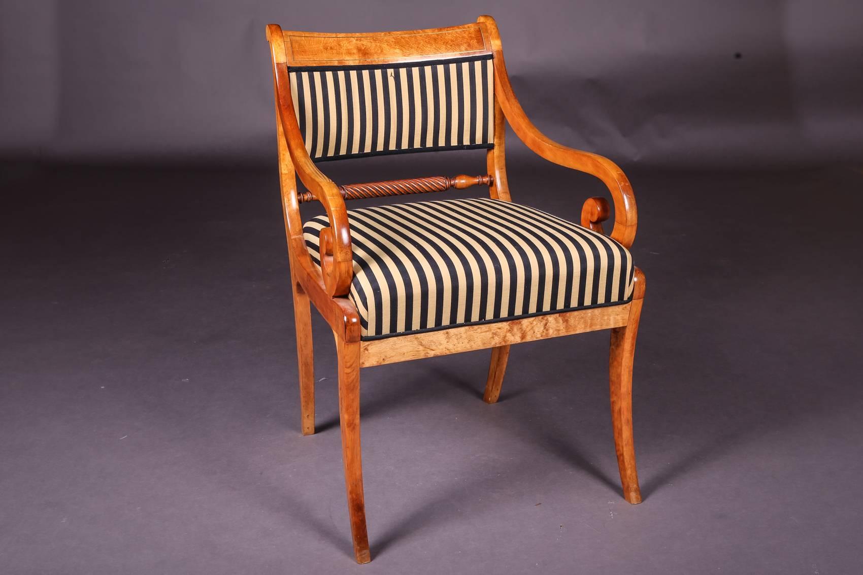 Solid birchwood. Trapezoidal frame on conical saber-shaped legs. Supports bracing supports for slightly rising armrests in rolled-up volute. High-arched curved backrest framing with wide end and a cord-shaped middle web. The armchair has been