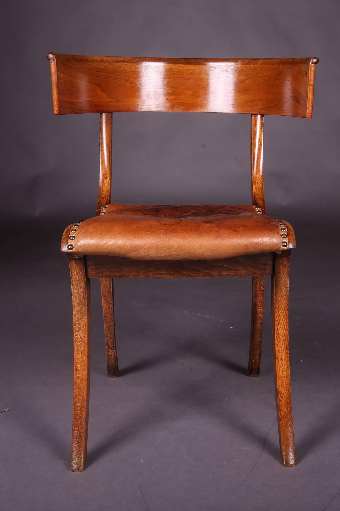 Chair of the Greek antique.
Solid wood. The striking shape with the wide-legged saber legs and the encircling backrest board was rediscovered in classicism, circa 1800. In this specimen, however, the pure basic form of the Klismos still exists. It