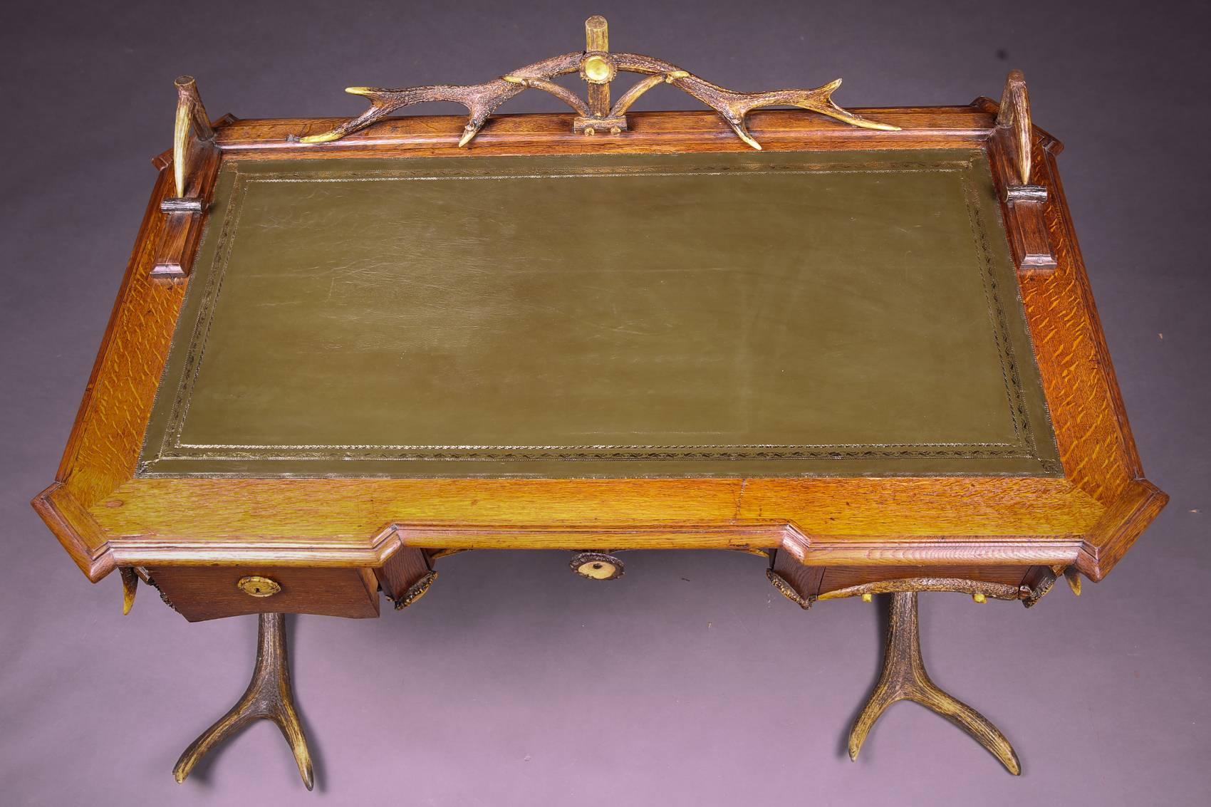 Musealer antique antler desk, circa 1840-1860.
Massive oak body on cross, linked feet. High knee pocket on the front with three drawers of different sizes. Antler decorated top. Extremely high-quality green leather plate with embossed gold