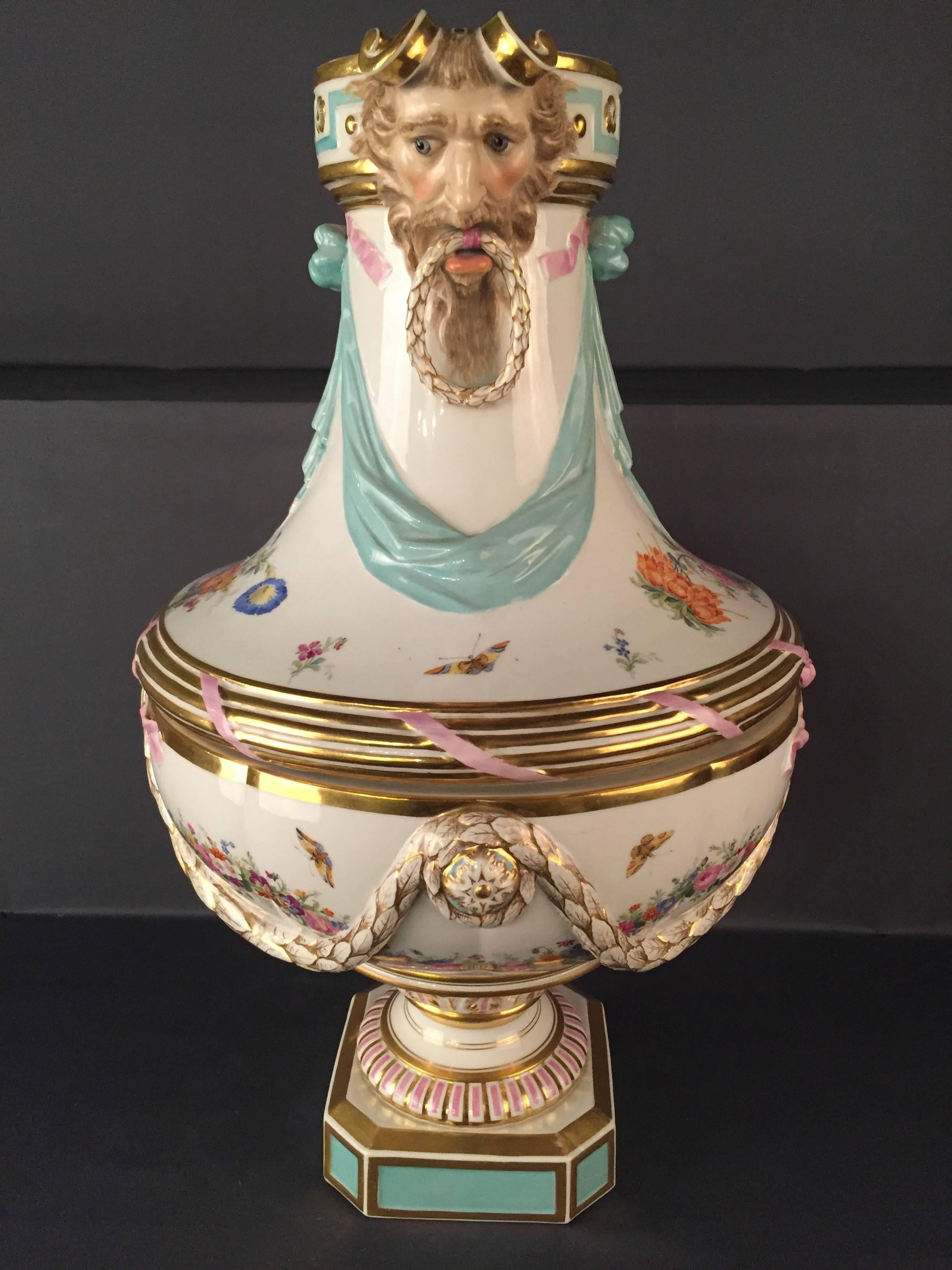 Vase with satyr heads. Urn shape with cloth draped on octagonal plinth.
Colorful painted flower garlands, bouquets, streublums and butterflies.
The satyr heads painted in color.
Pink, light green and gold stained. Gold edges.
Blue scepter brand.