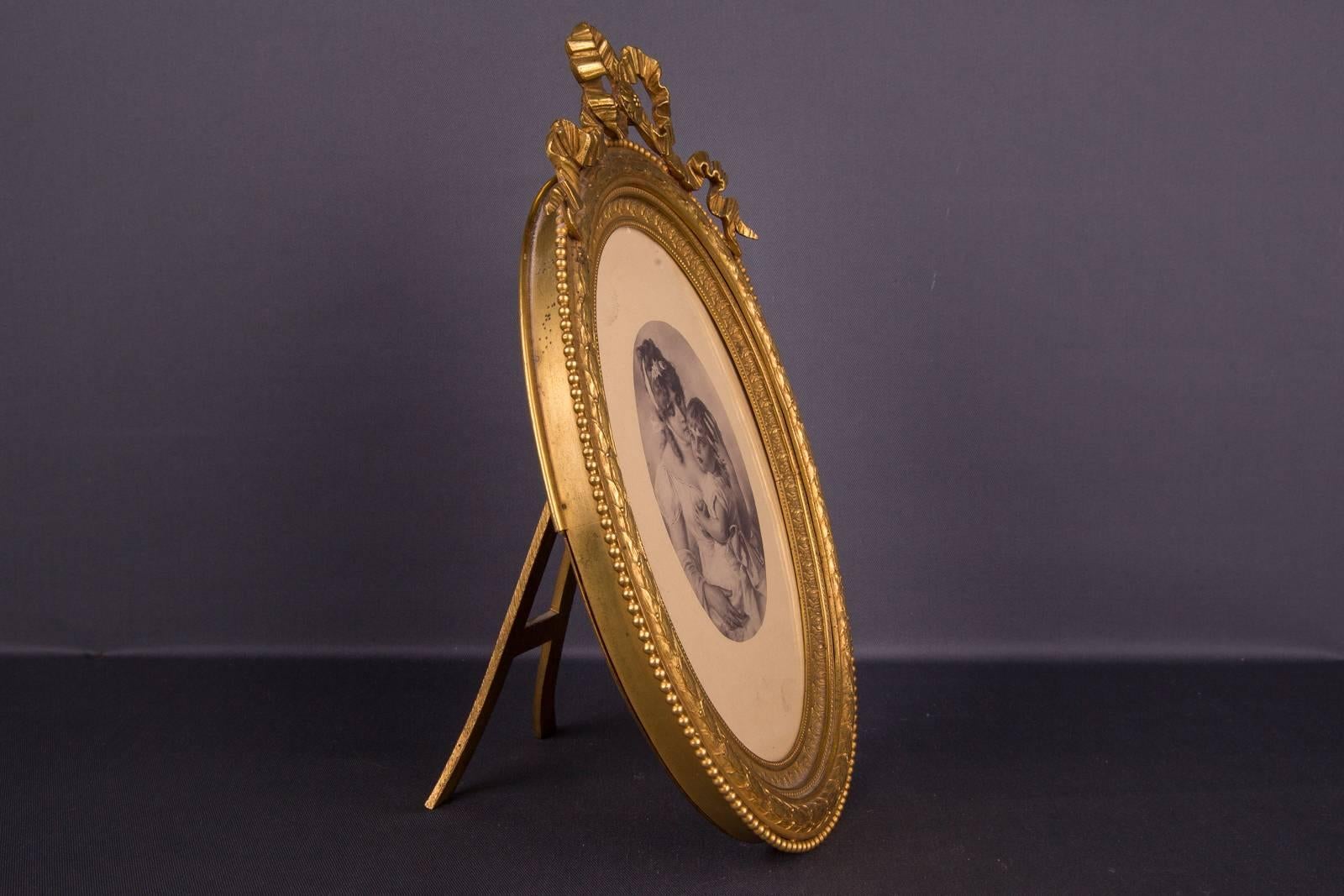 Oval body. Extremely finely chiselled bronze fire gilding. Picture frame, crowned with the typical loops of the Louis Seize. Richly chiselled and profiled edge. Framed with a beaded edge. In the back an A-shaped Stand. Above the frame is an eyelet