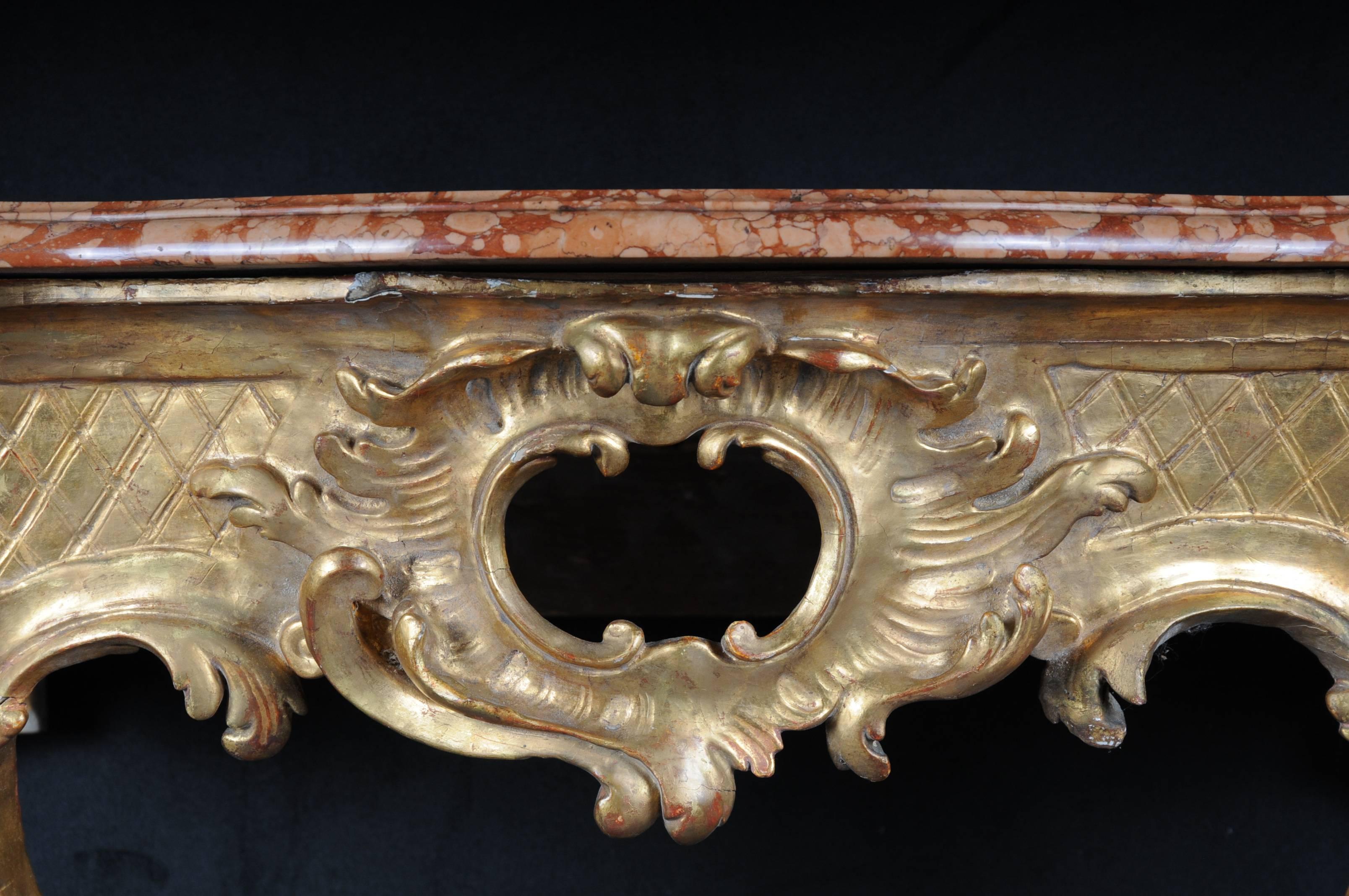 Baroque console table. Wood, gilded. Frame with openwork cartridge. Two opposing C-rocailles with bracing. Cut red marble slab. France.



(E-34).
