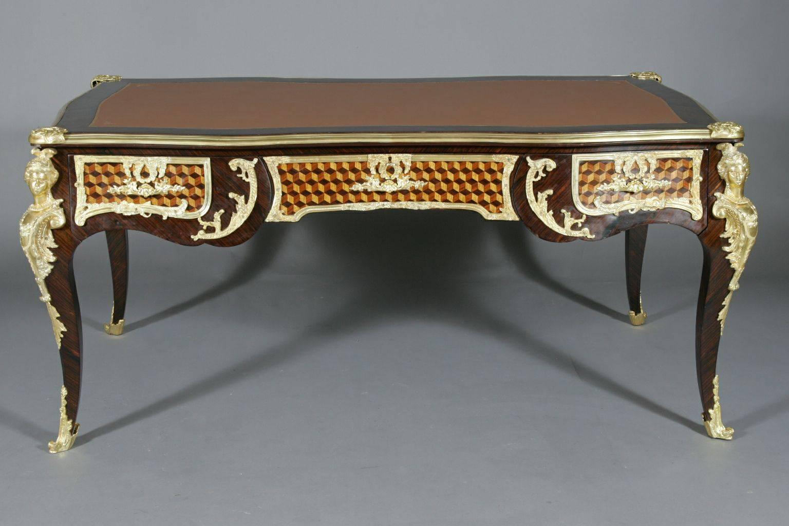 Monumental French bureau plat in Louis XV style.
Tulip veneer on solid pinewood. Cube marquetry inlaid with finely engraved brass fixtures. On a slope, two forward glancing, impressive female busts on curved legs. Highly decorative Brass fittings